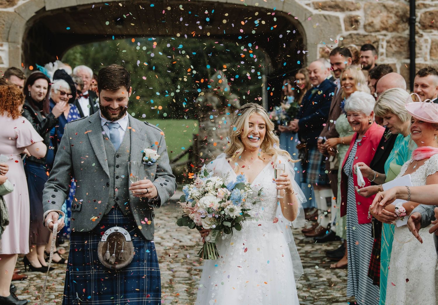 Joyful bride and groom exit ceremony through confetti shower surrounded by cheering wedding guests.