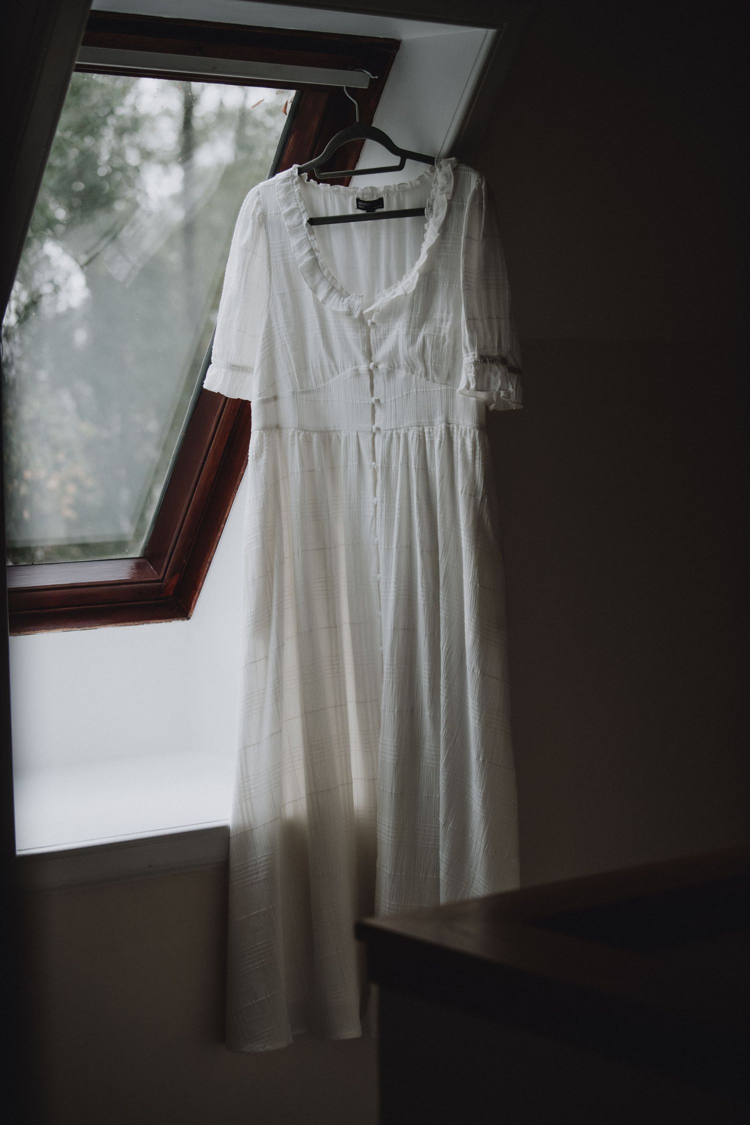 Elegant white wedding dress with ruffled neckline and short sleeves hanging in a window.
