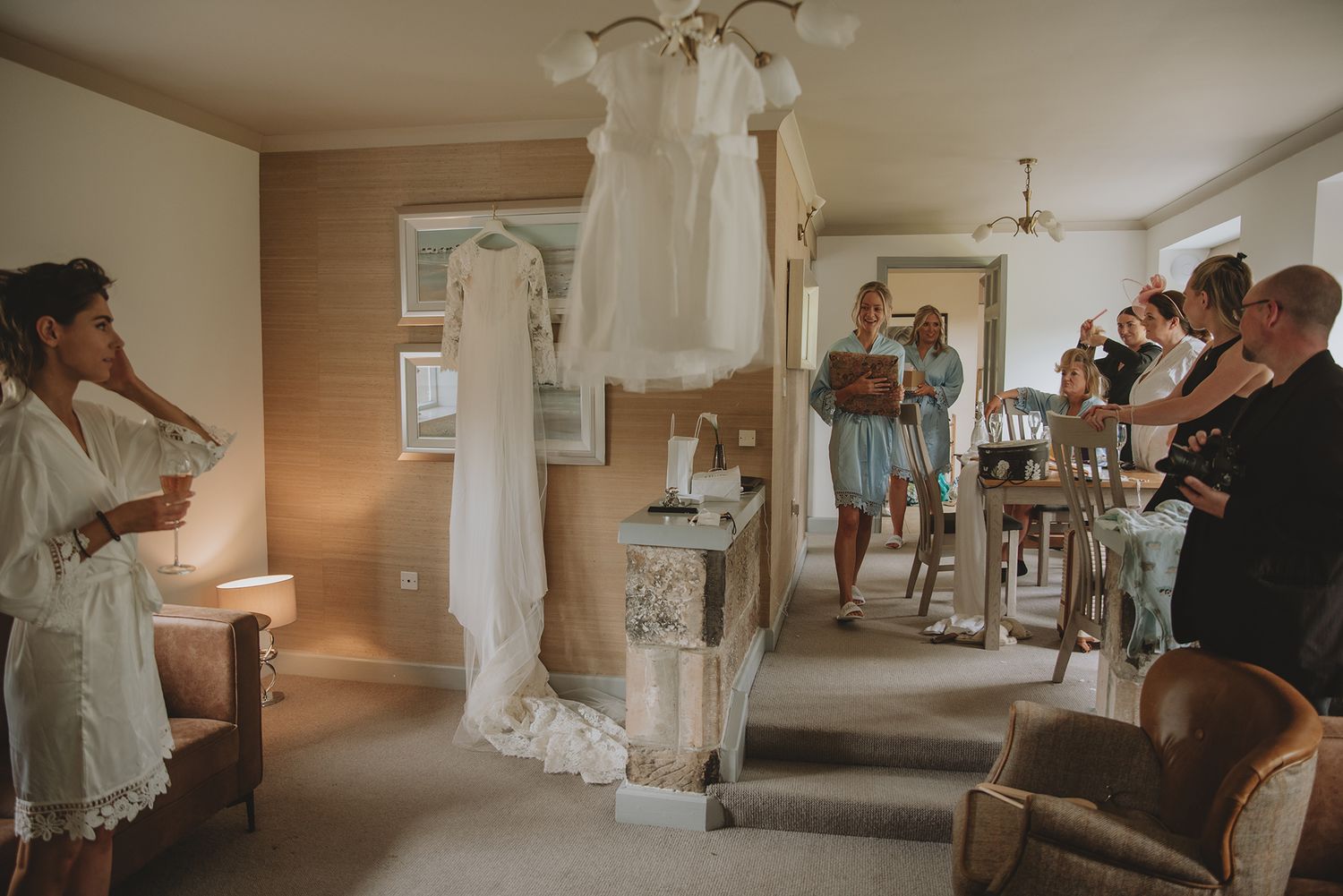 Bridal party admiring wedding dress hanging in room during wedding preparations.