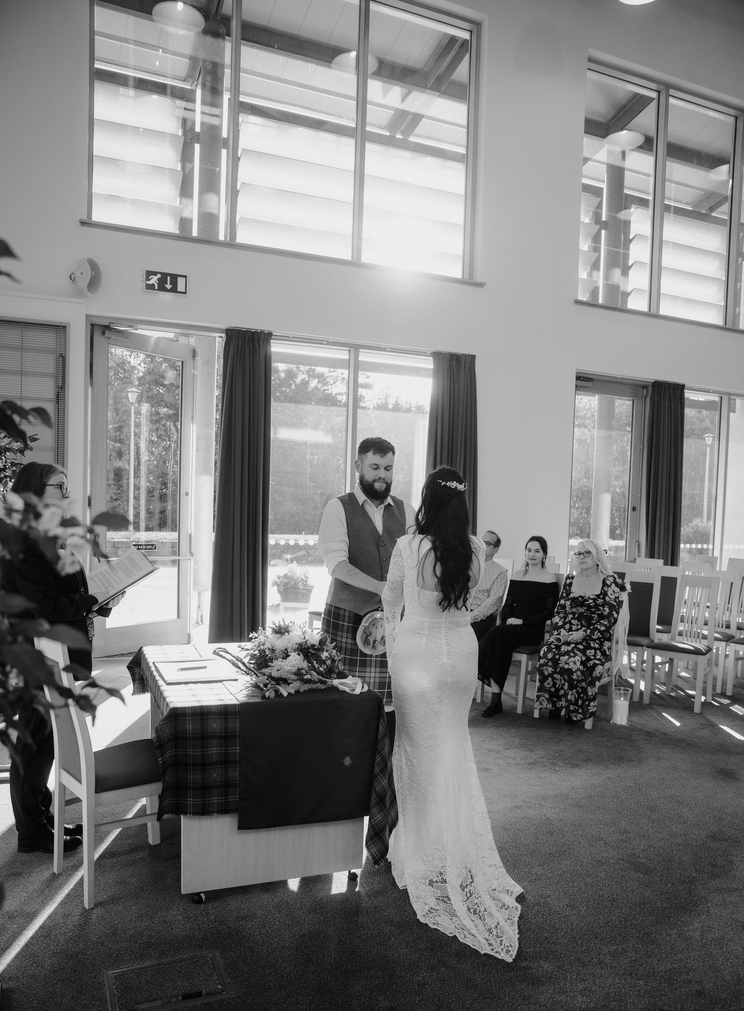 Bride and groom exchange vows at altar in bright modern ceremony venue in black and white photo.