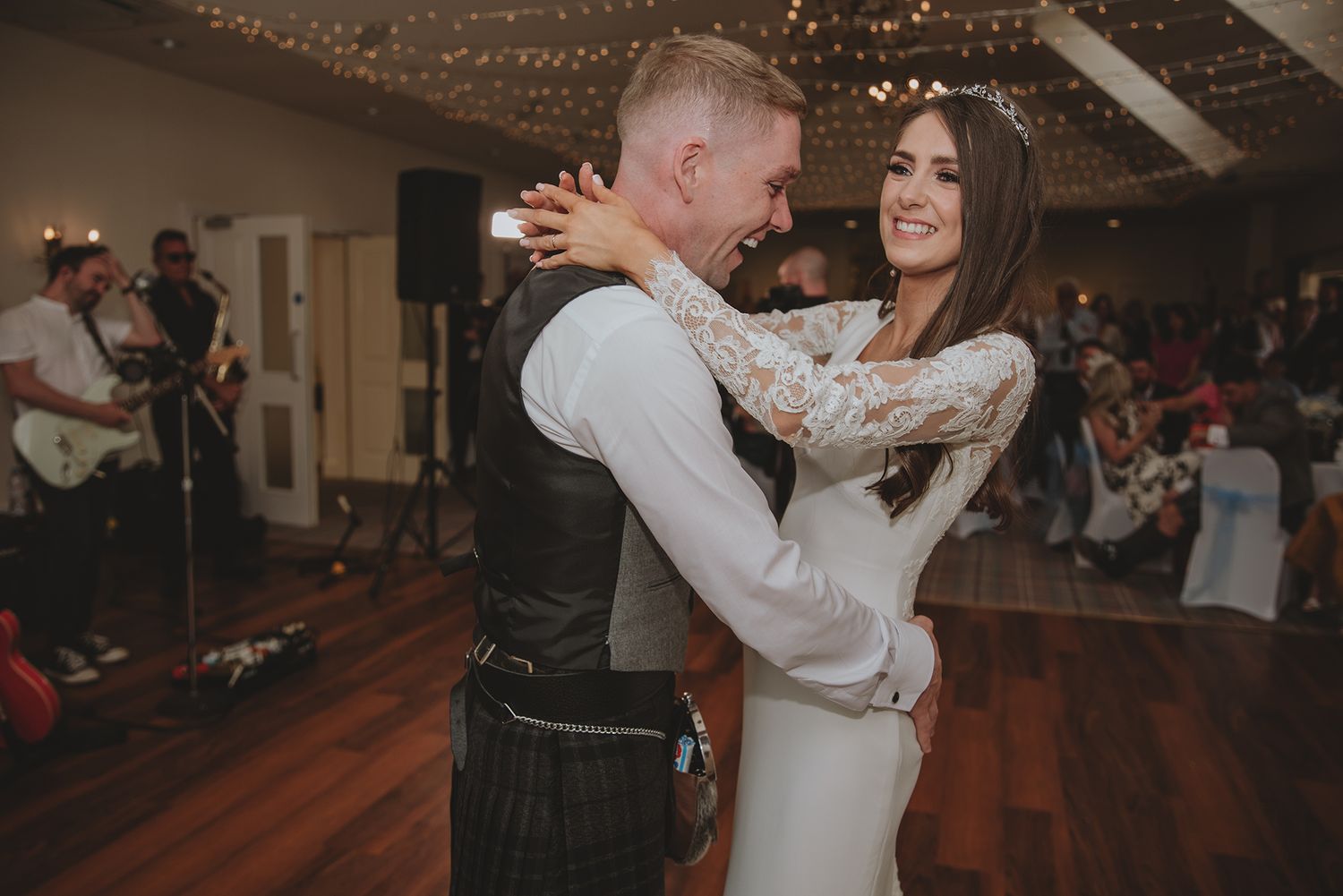 Smiling bride and groom sharing a joyful first dance, groom in Scottish kilt at elegant wedding reception.