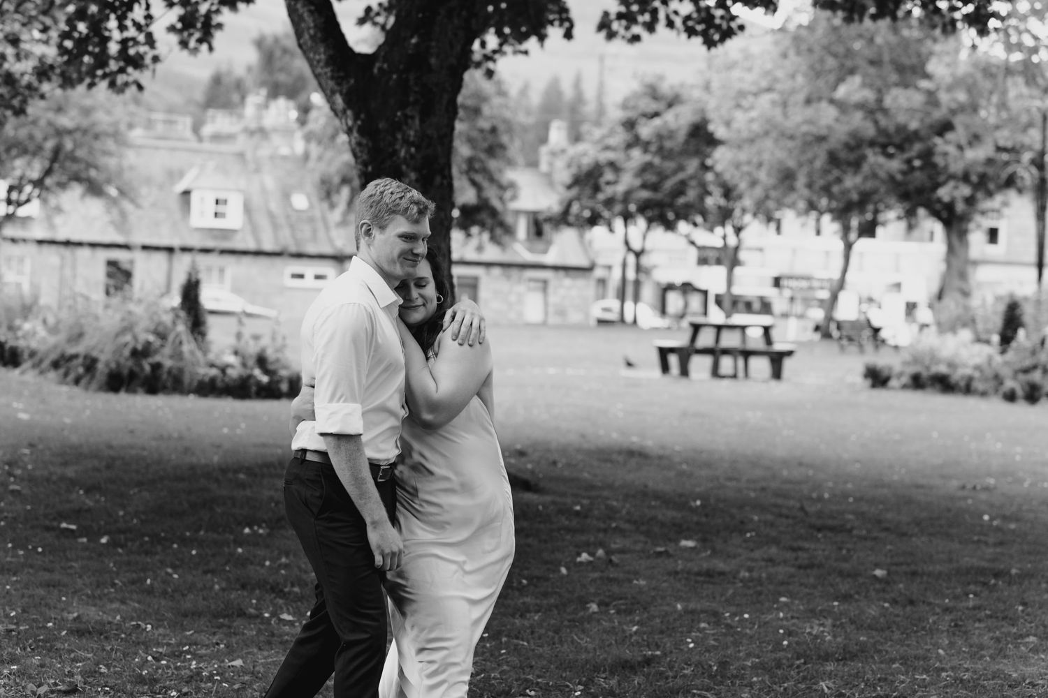 Black and white photo of a couple embracing outdoors in a park, sharing a tender romantic moment.