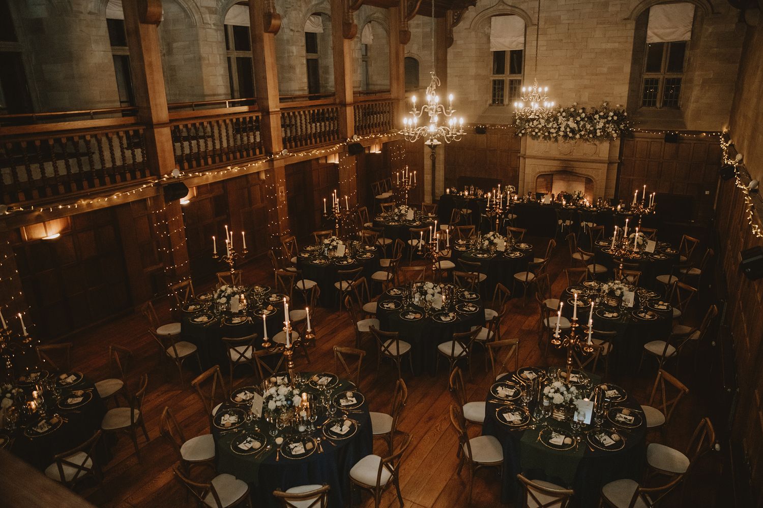 Elegant wedding reception in a historic castle venue with candlelit round tables, chandeliers, and warm ambient lighting.