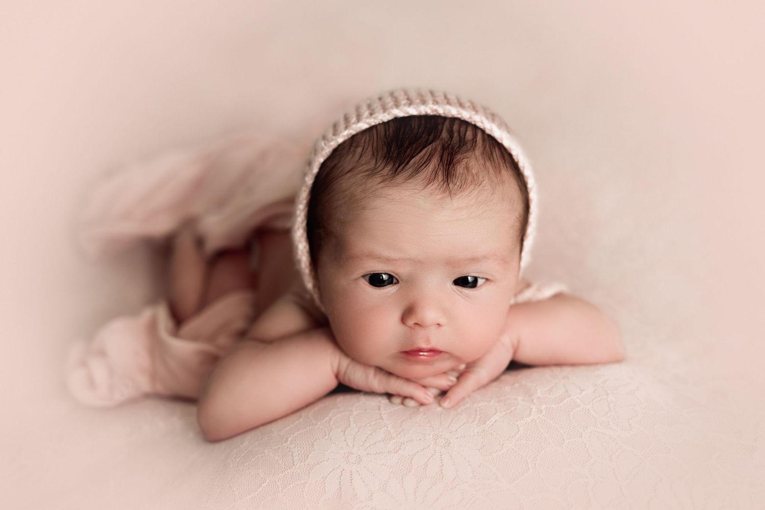 Newborn girl in pink knit bonnet with her chin resting on her hands during luxury newborn photography session at The Essence Photography.