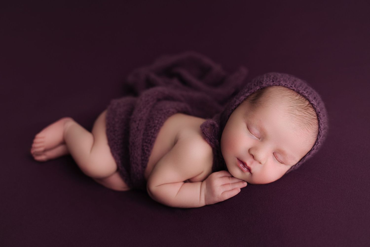 Beautiful newborn baby girl photo session. Baby girl is posed on her side with hand tucked under her chin and knees bent and feet together.
