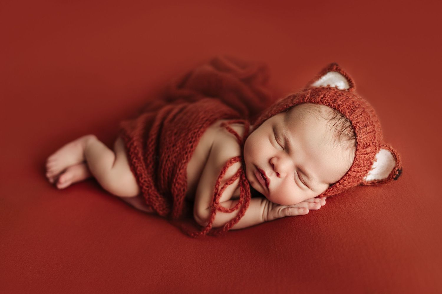 Newborn baby boy wearing cute fox knit hat posed on deep terracotta orange during styled newborn photo session at The Essence Photography.