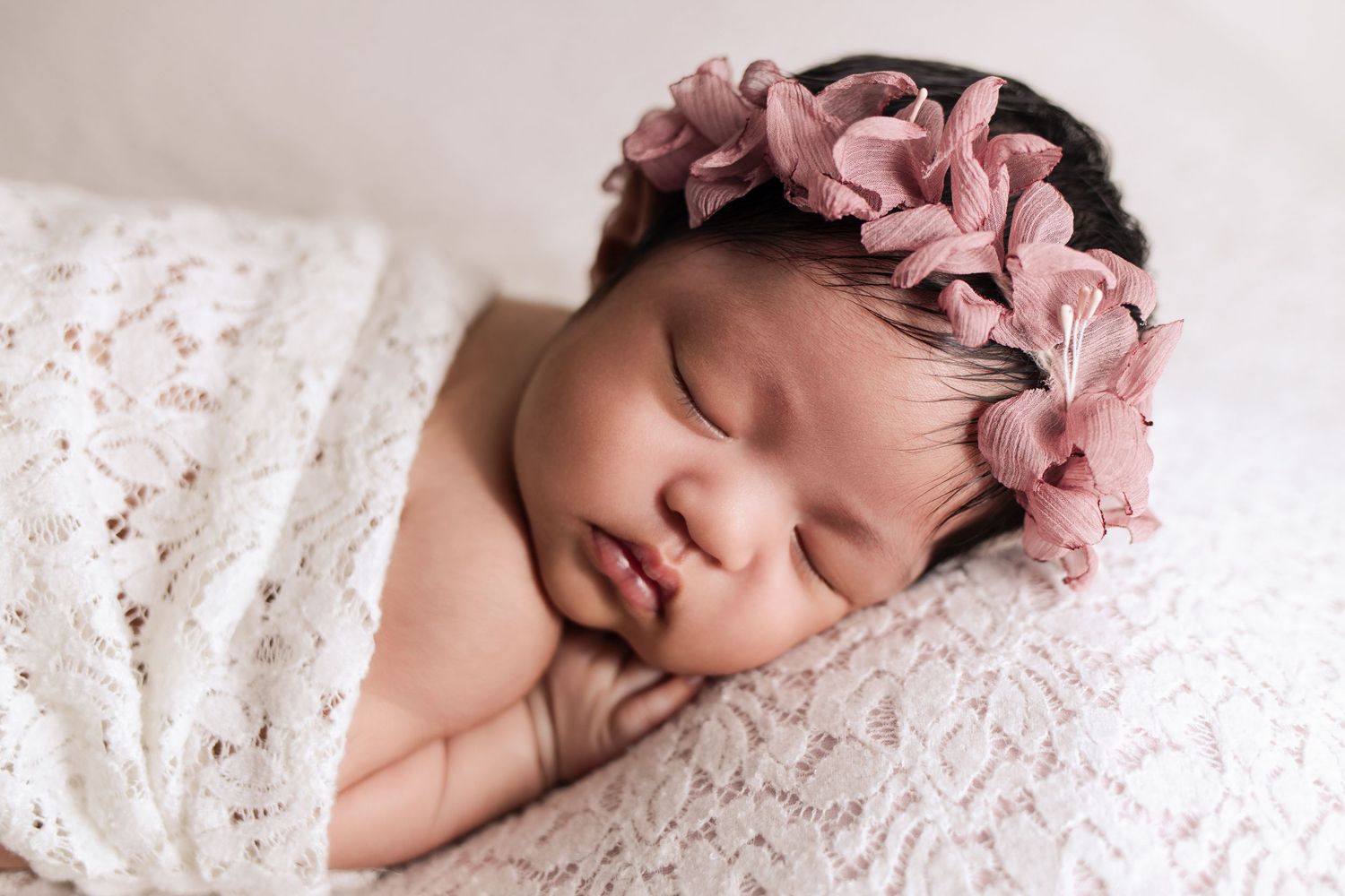 Closeup of newborn baby wrapped in lacy blanket with cute floral headband at The Essence Photography, luxury newborn photography studio.