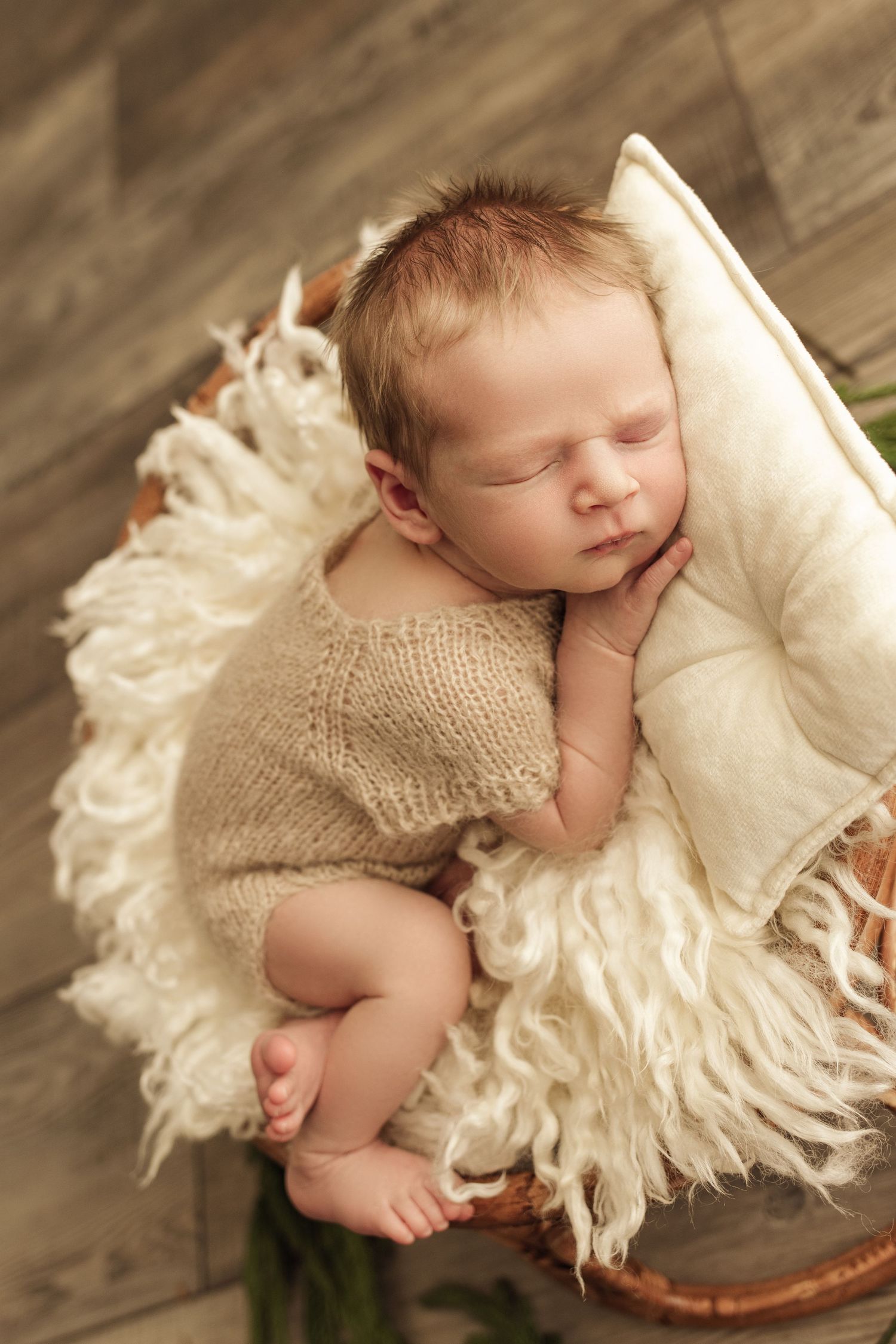 Newborn photography session. Baby boy is curled up on mini bamboo papasan chair with hand tucked under his cheek, and feet crossed over.
