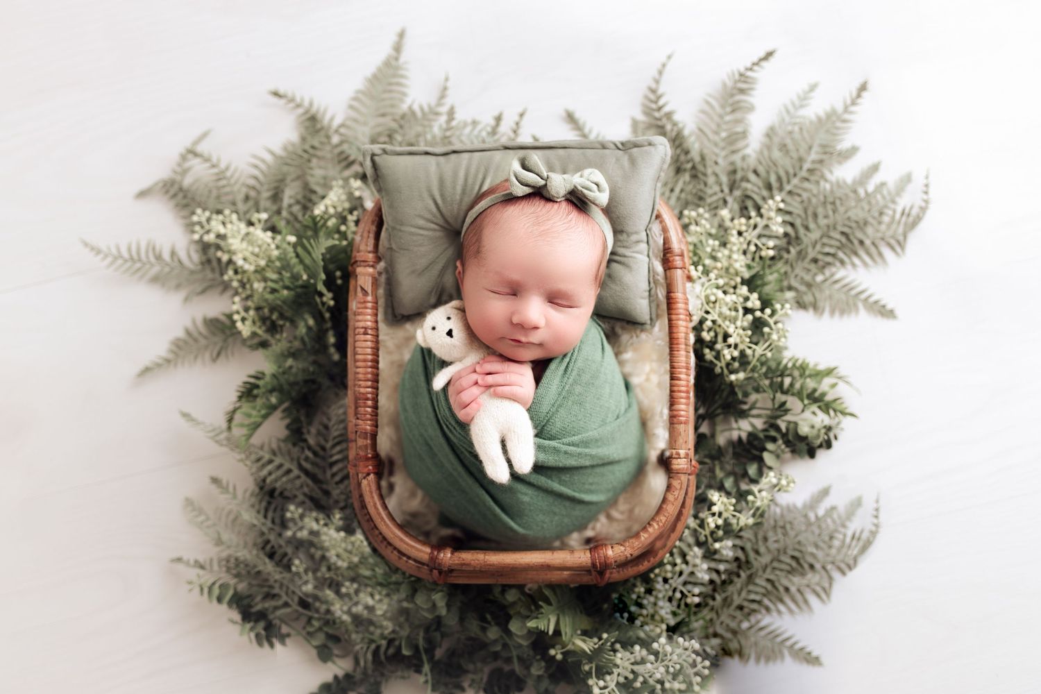 Adorable newborn swaddled and nestled into bamboo basket surrounded by florals and greens during luxury newborn photo shoot in Radium, BC.