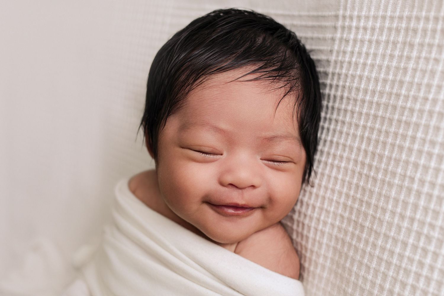 A newborn smiles sweetly in her sleep at a lifestyle newborn session at The Essence Photography studio in Radium Hot Springs, BC.