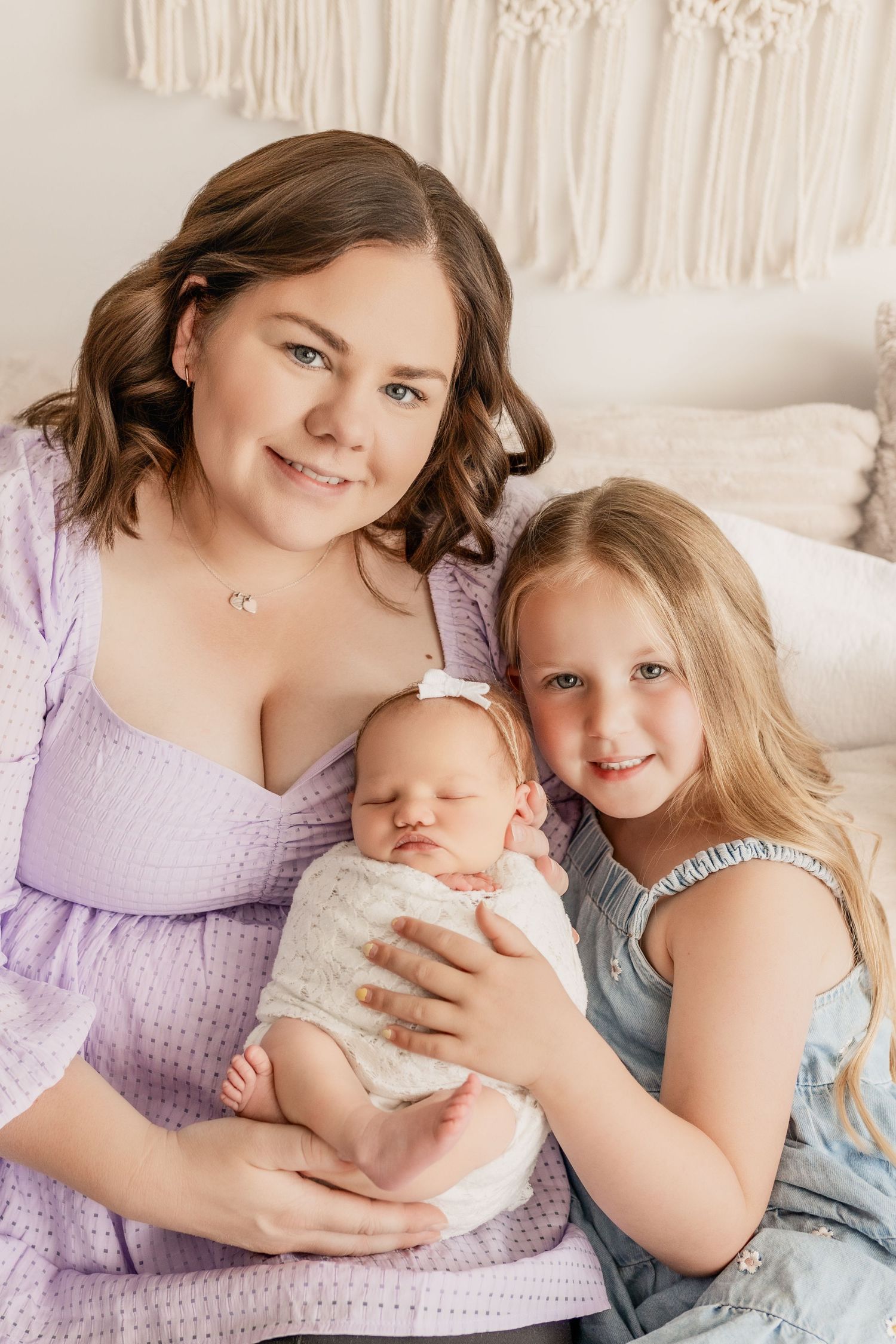 A mother with her newborn and older daugther snuggled together during a photo session The Essence Photography studio in Radium Hot Springs.