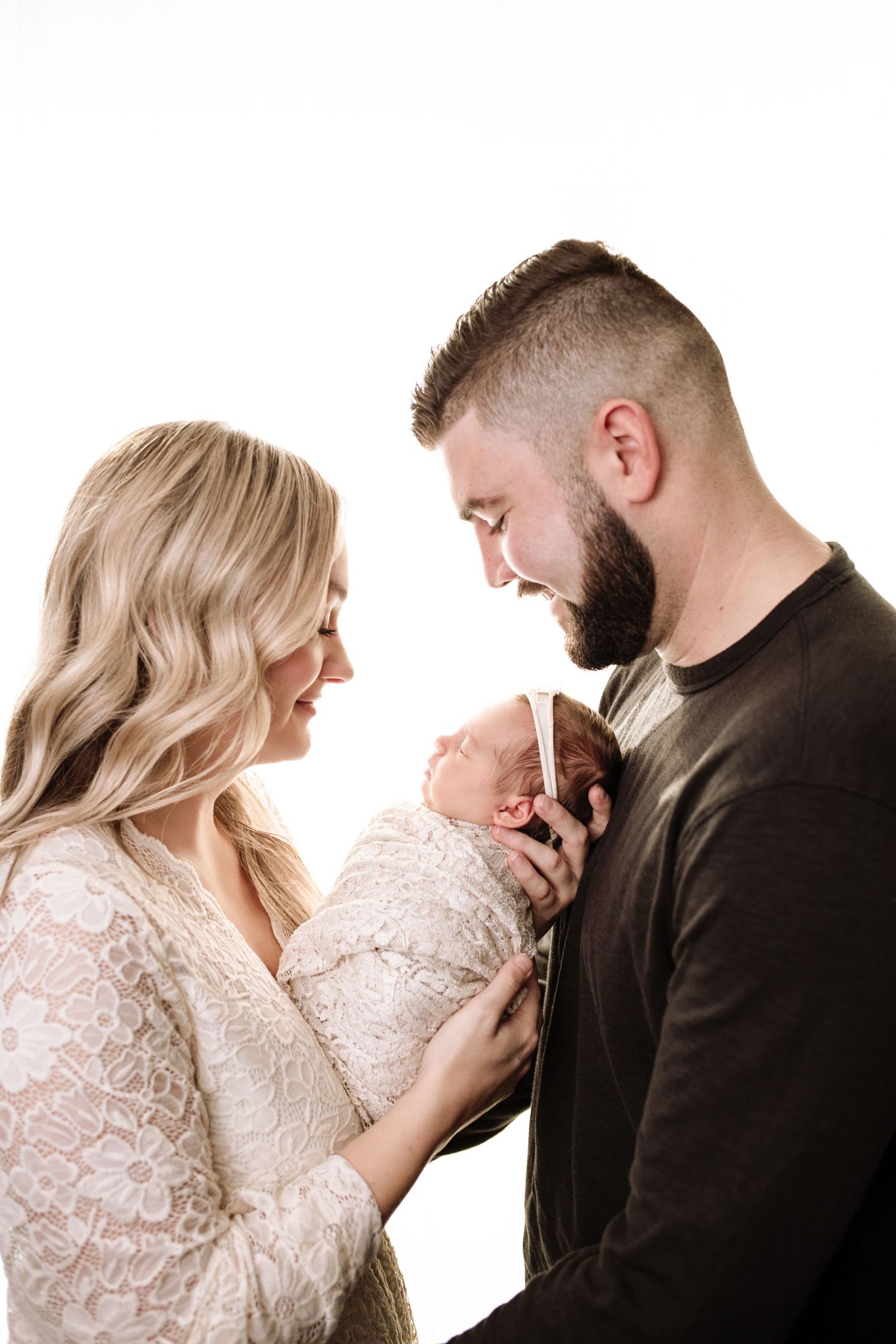 Newborn and family photography session. Mom holds baby facing her and dad faces mom, both look down at baby. Beautiful profile photo.