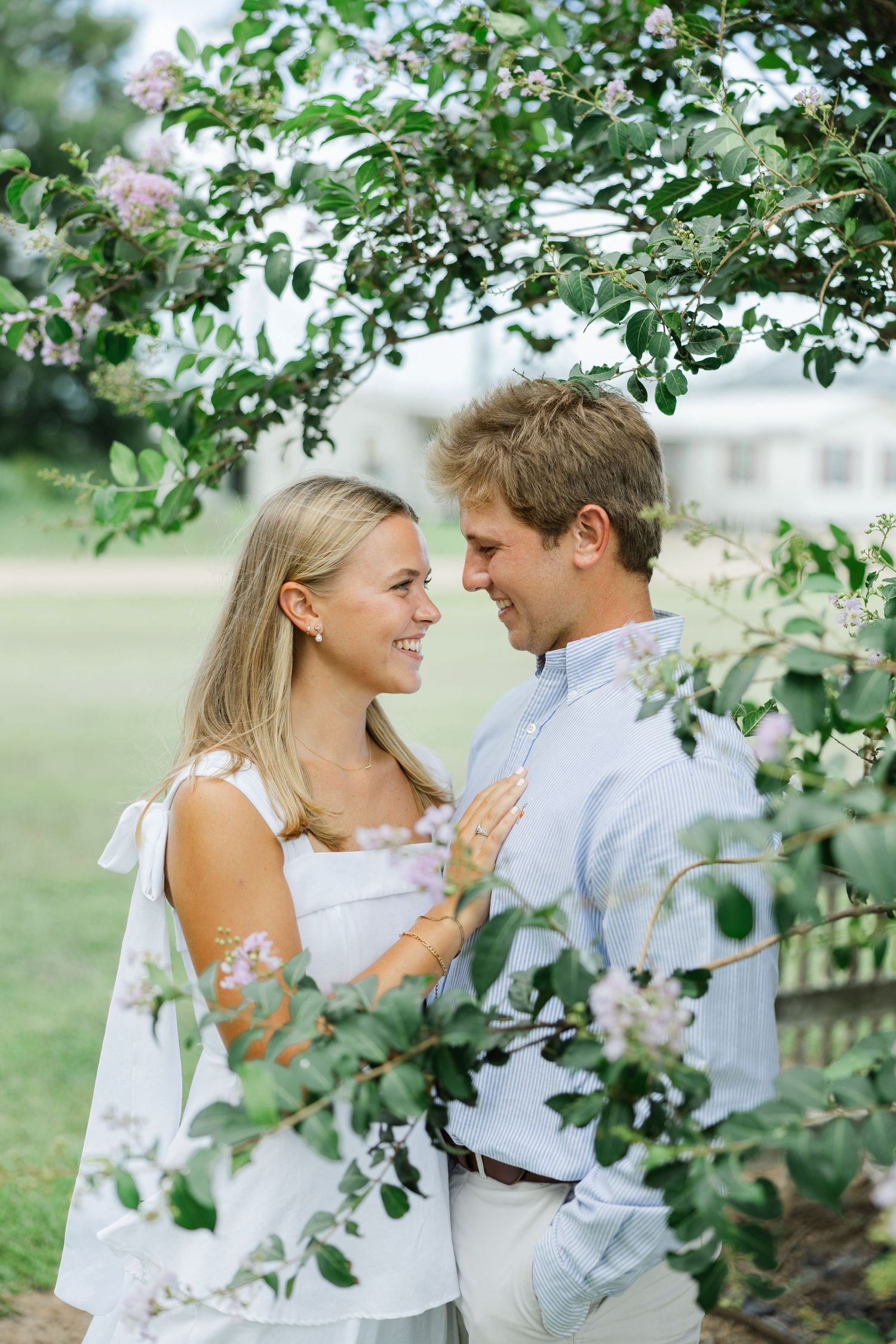 Happy couple smiling at each other framed by flowering branches with soft green garden backdrop.