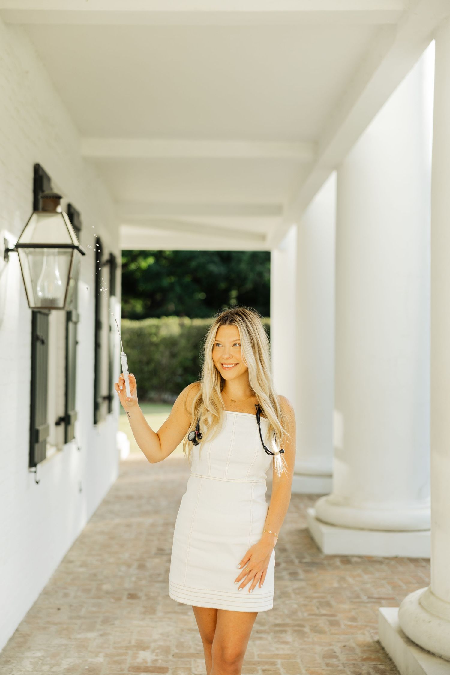 Blonde woman in white mini dress walking along elegant white columned outdoor corridor.