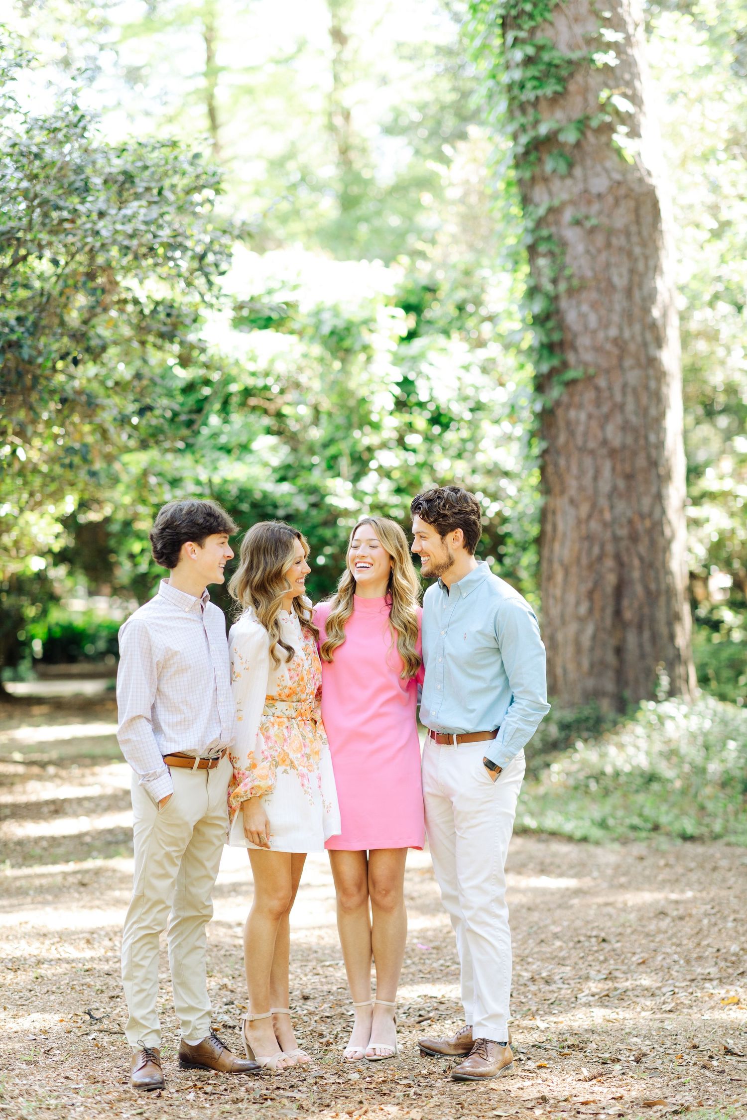 Four young adults in pastel spring outfits smiling together on a sun-dappled garden path.