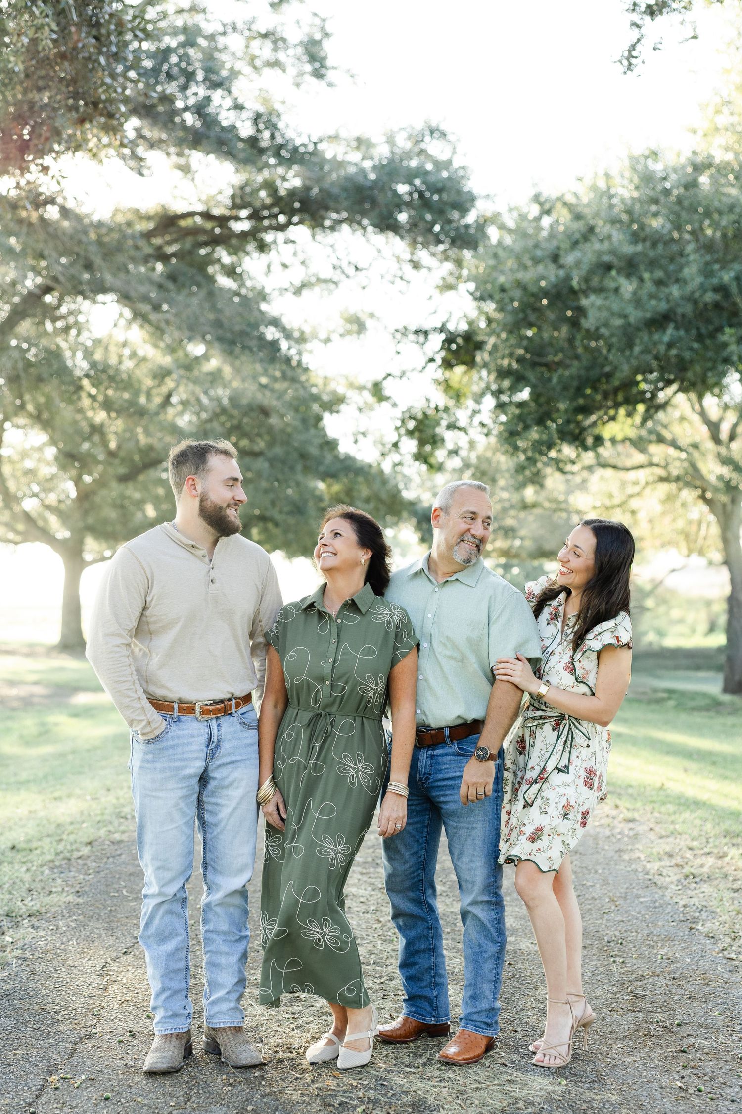 Family of four posing outdoors on a tree-lined path in fall attire.