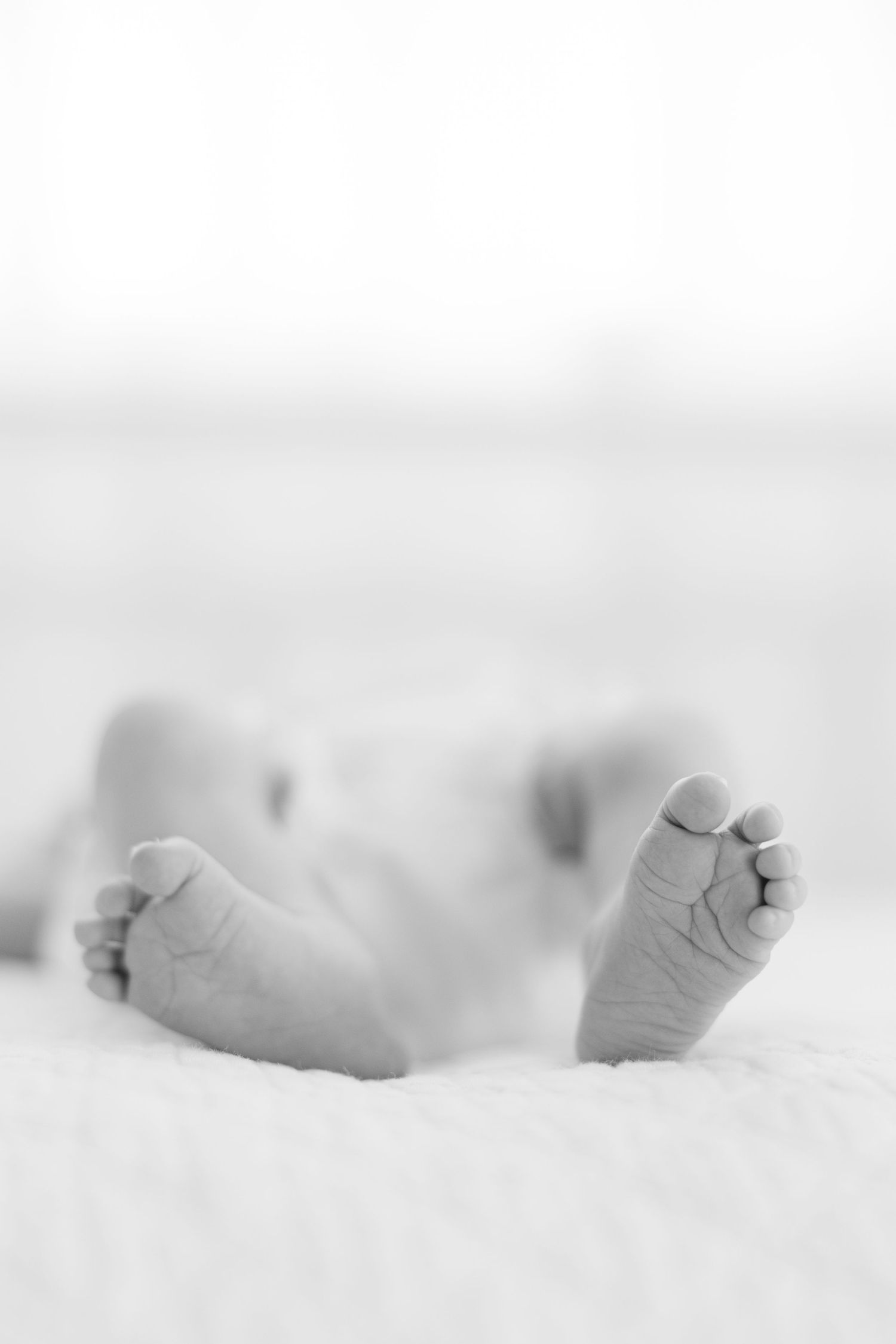 Sleeping newborn baby swaddled in white with a pink gingham bow in a white wicker bassinet.