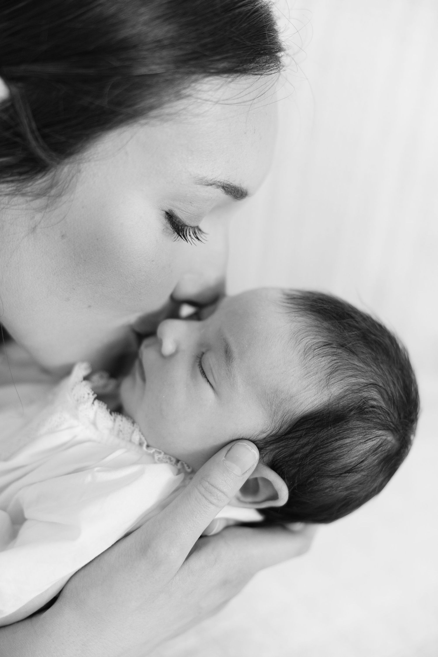 Black and white photo of a mother gently kissing her sleeping newborn baby.
