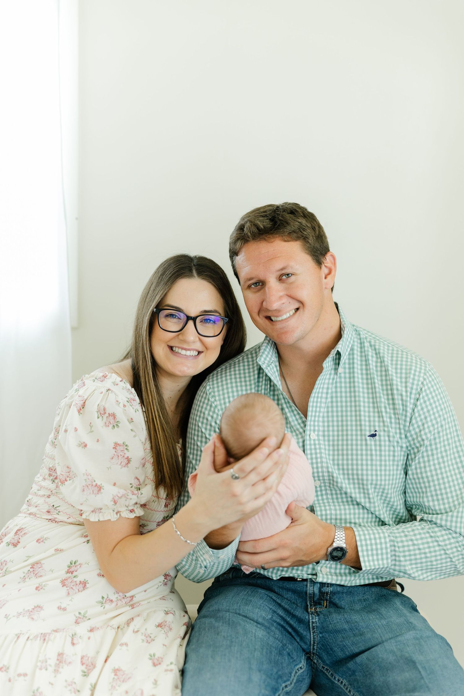 Happy parents smiling while holding their newborn baby dressed in pink.