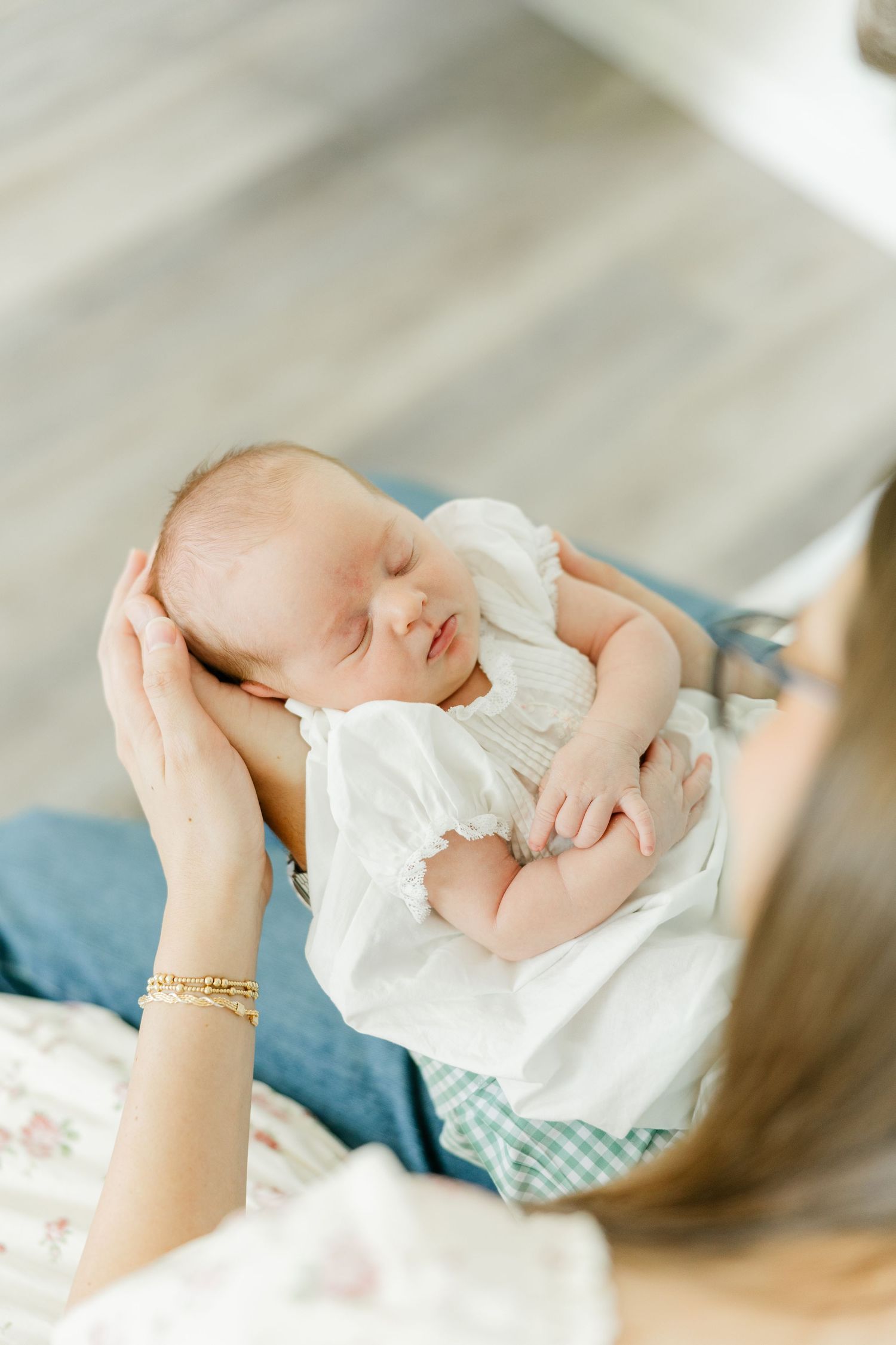 Mother gently cradling her sleeping newborn baby dressed in a white outfit, viewed from above.