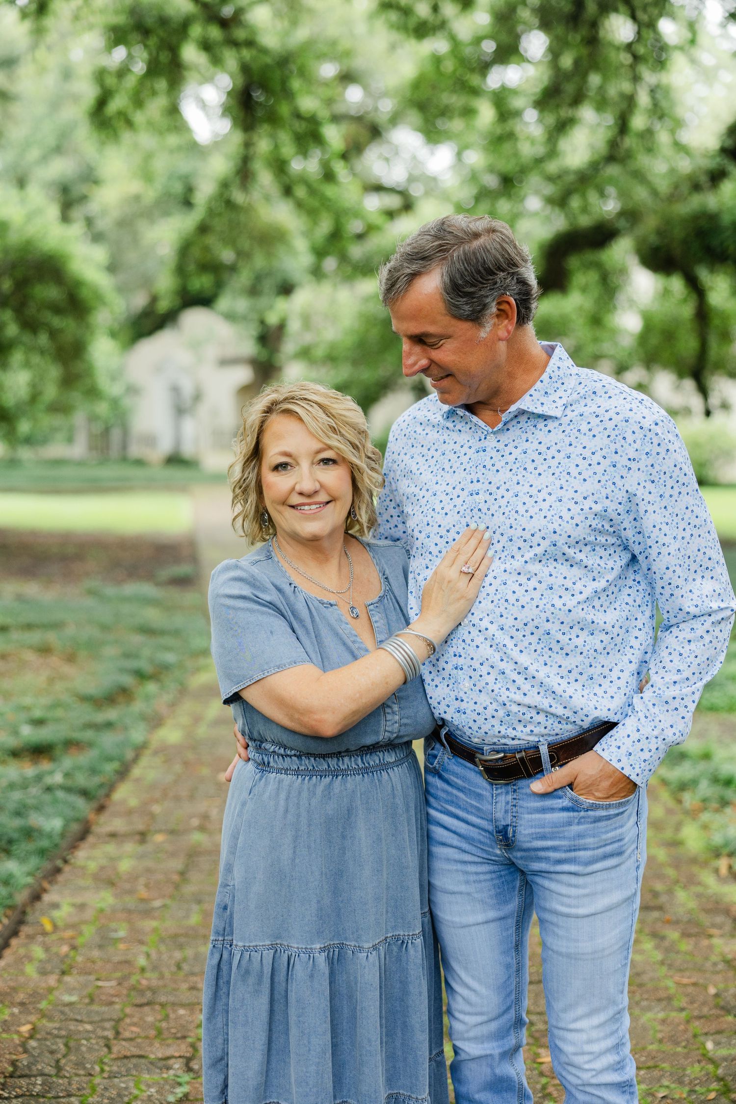 Smiling middle-aged couple in blue outfits posing together on a garden pathway.