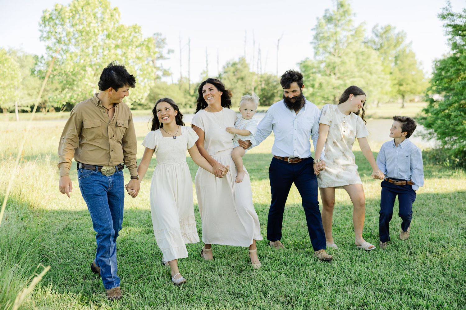 Extended family walking together holding hands on green lawn outdoors.