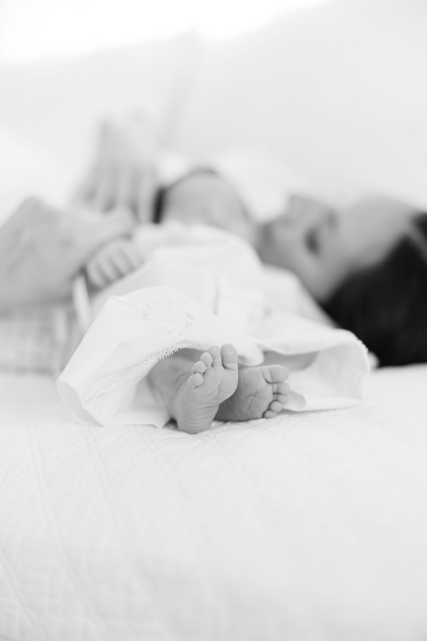 Black and white close-up of newborn baby feet with mother resting peacefully in background.