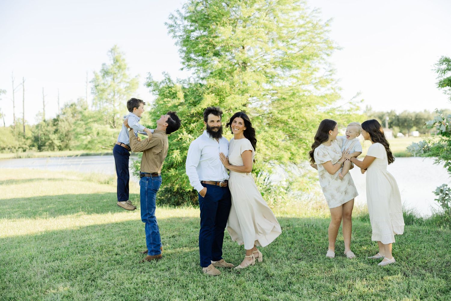 Two families gathered on green lawn posing for outdoor portrait session.