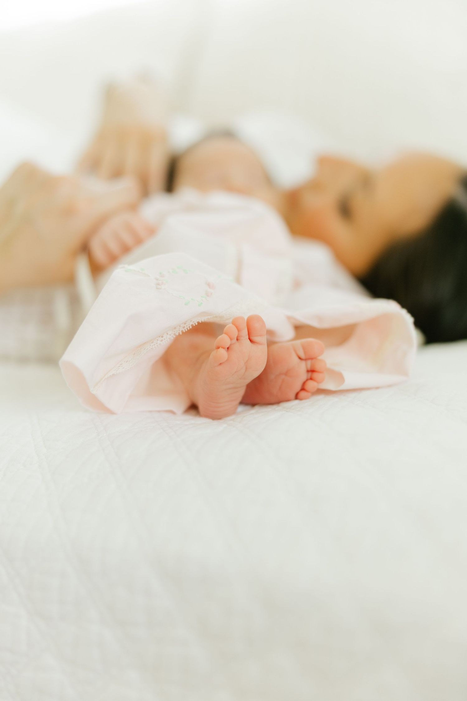 Close-up of a sleeping newborn baby's tiny feet in a pink outfit on a white bed.