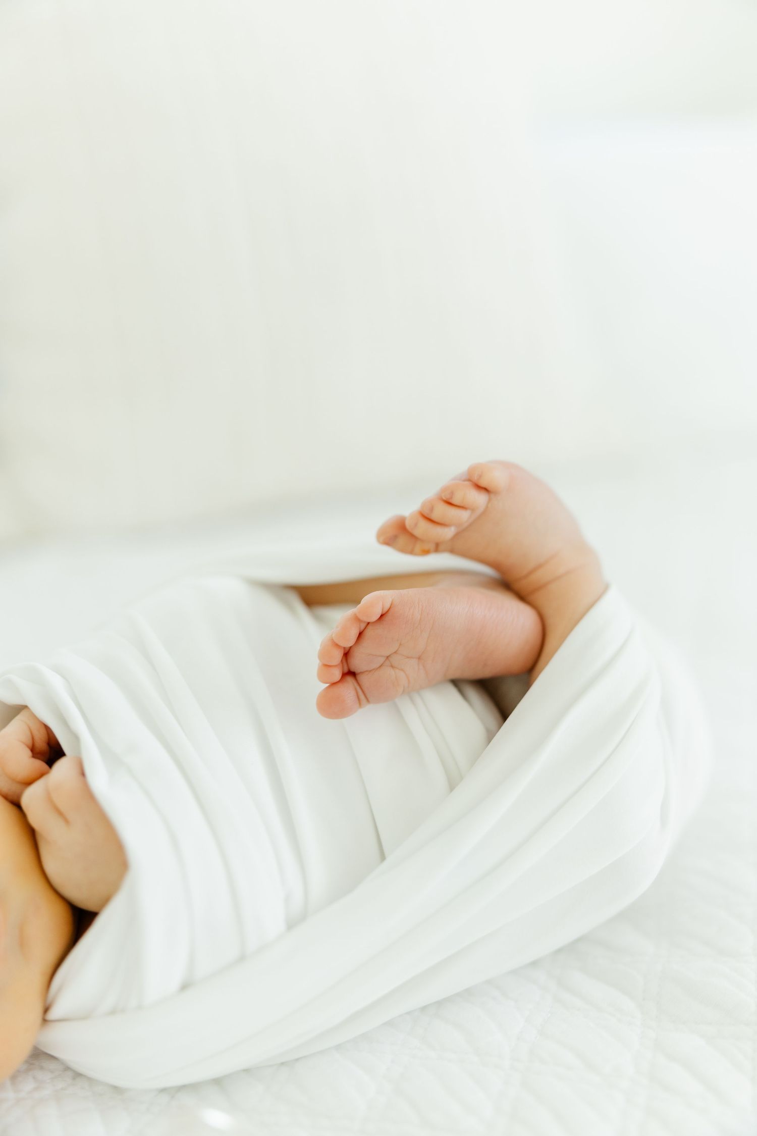 Close-up of newborn baby tiny feet peeking out from a white swaddle blanket.