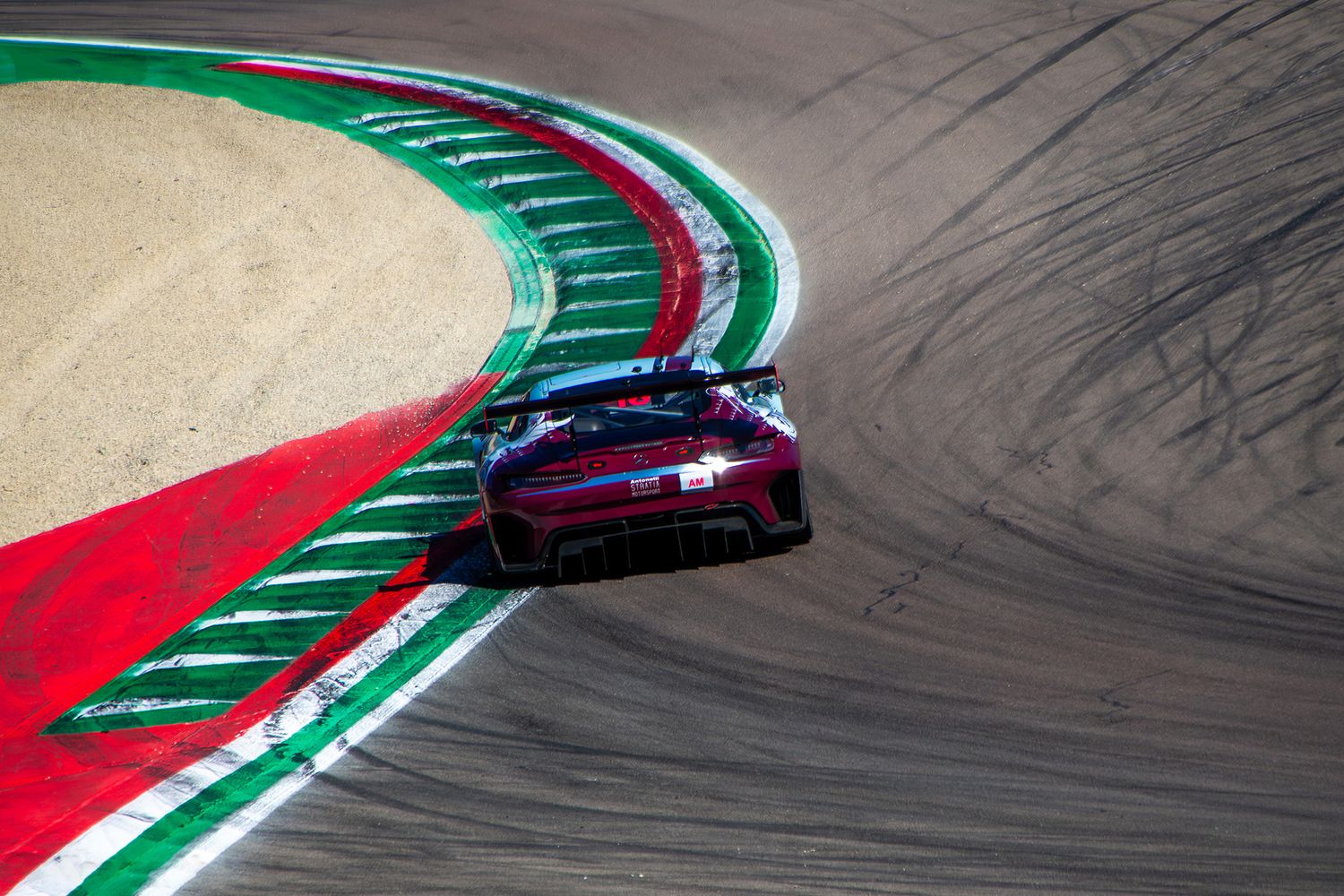 High angle shot of a Mercedes GT3 racing car cornering over the prominent tricolor green, white, and red curb.