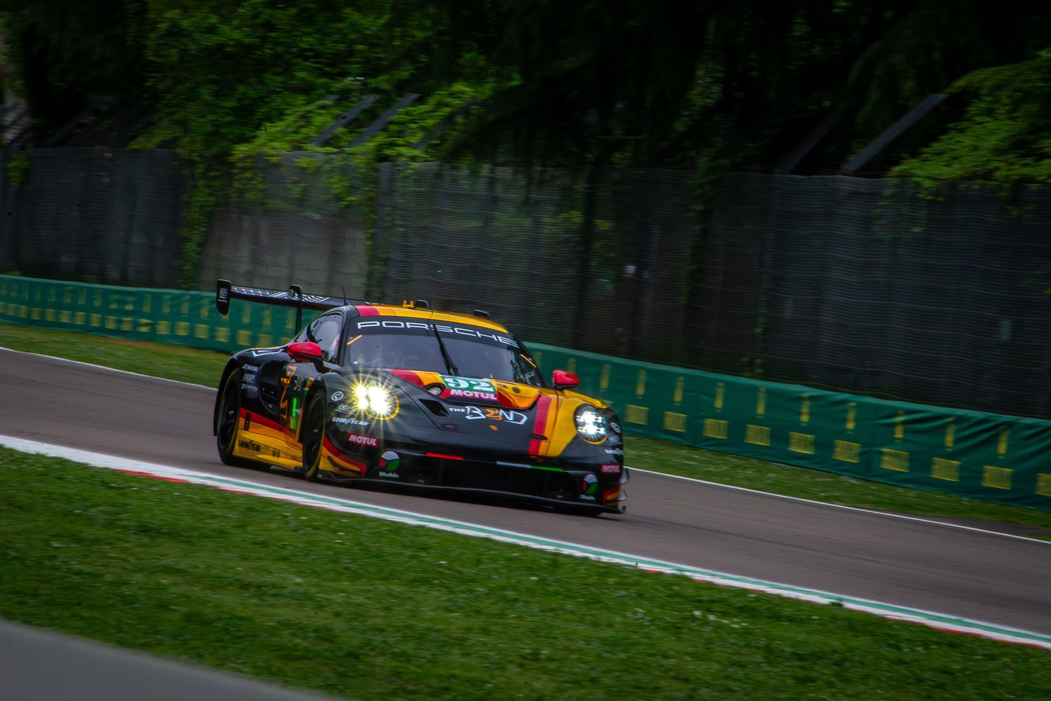 Black and yellow Porsche GT3 car driving on the track at Imola circuit, framed by the forest.