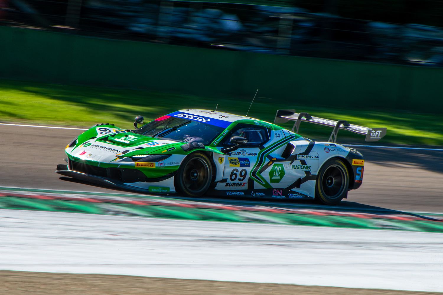 Panning shot of a green and white Ferrari GT3 racing car cornering over a tricolor curb at Imola.