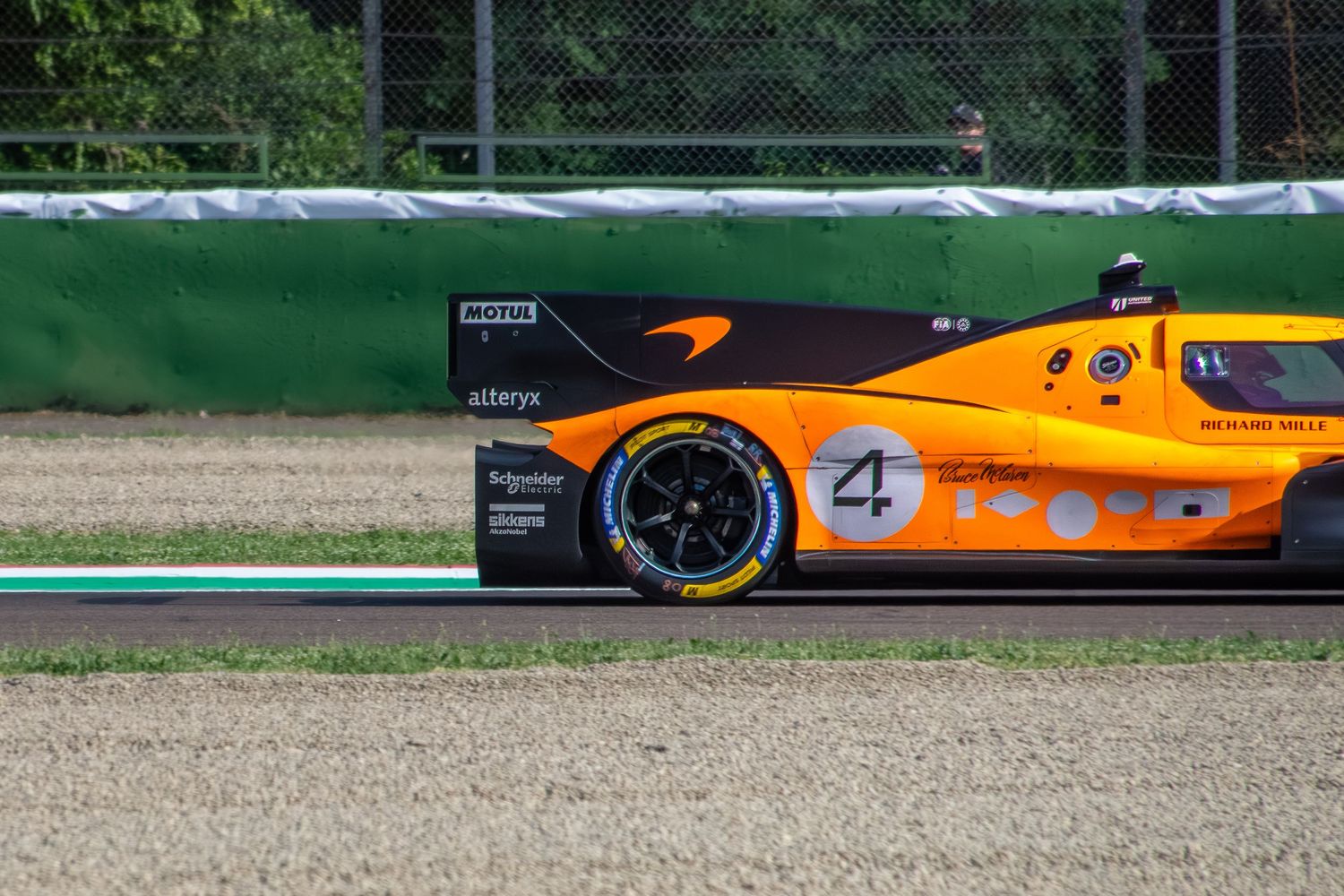 Close-up side profile of the rear section and rear tire of the orange and black number 4 racing car on the track.