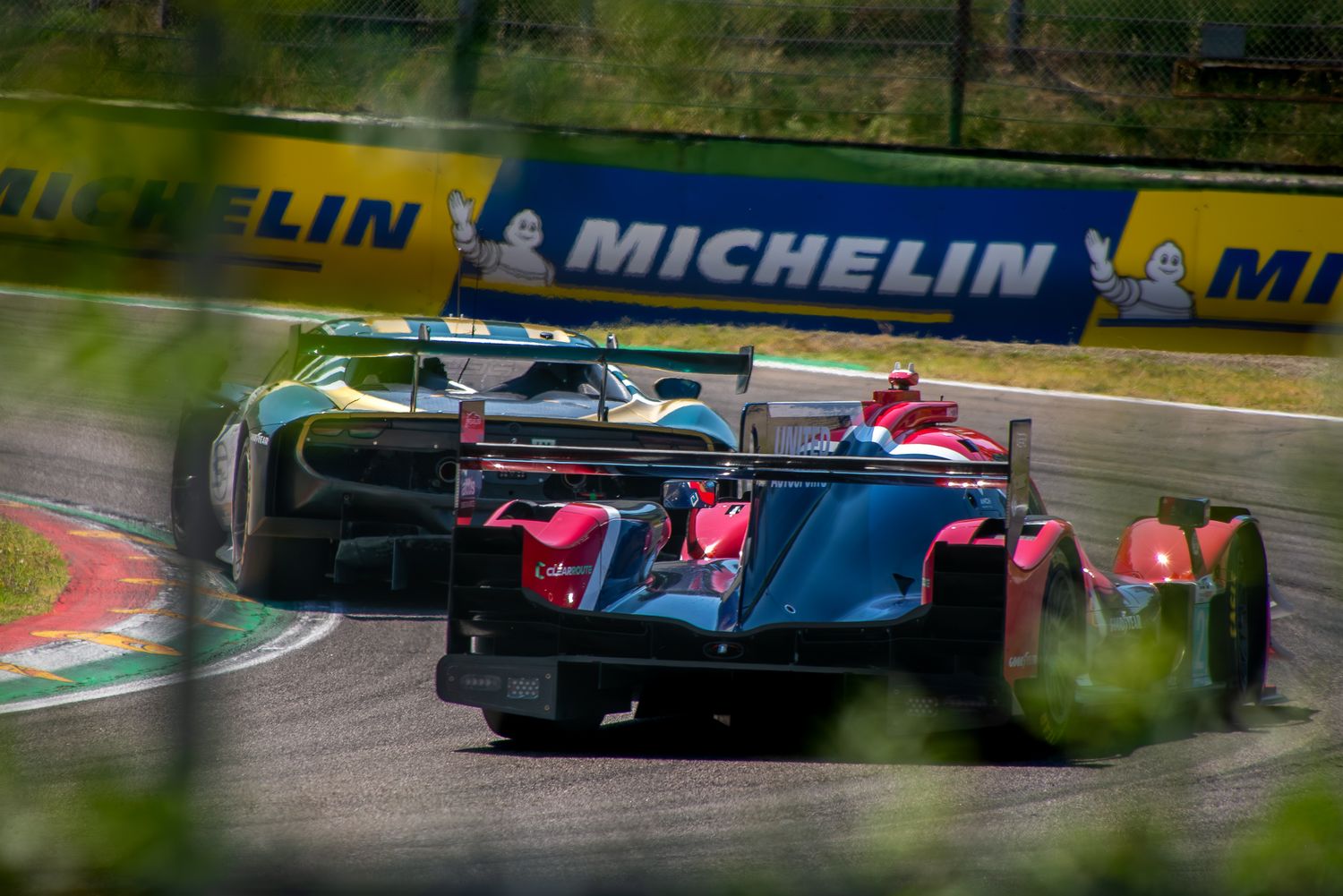 Rear view of two endurance racing cars battling for position on a track corner with Michelin banners behind.