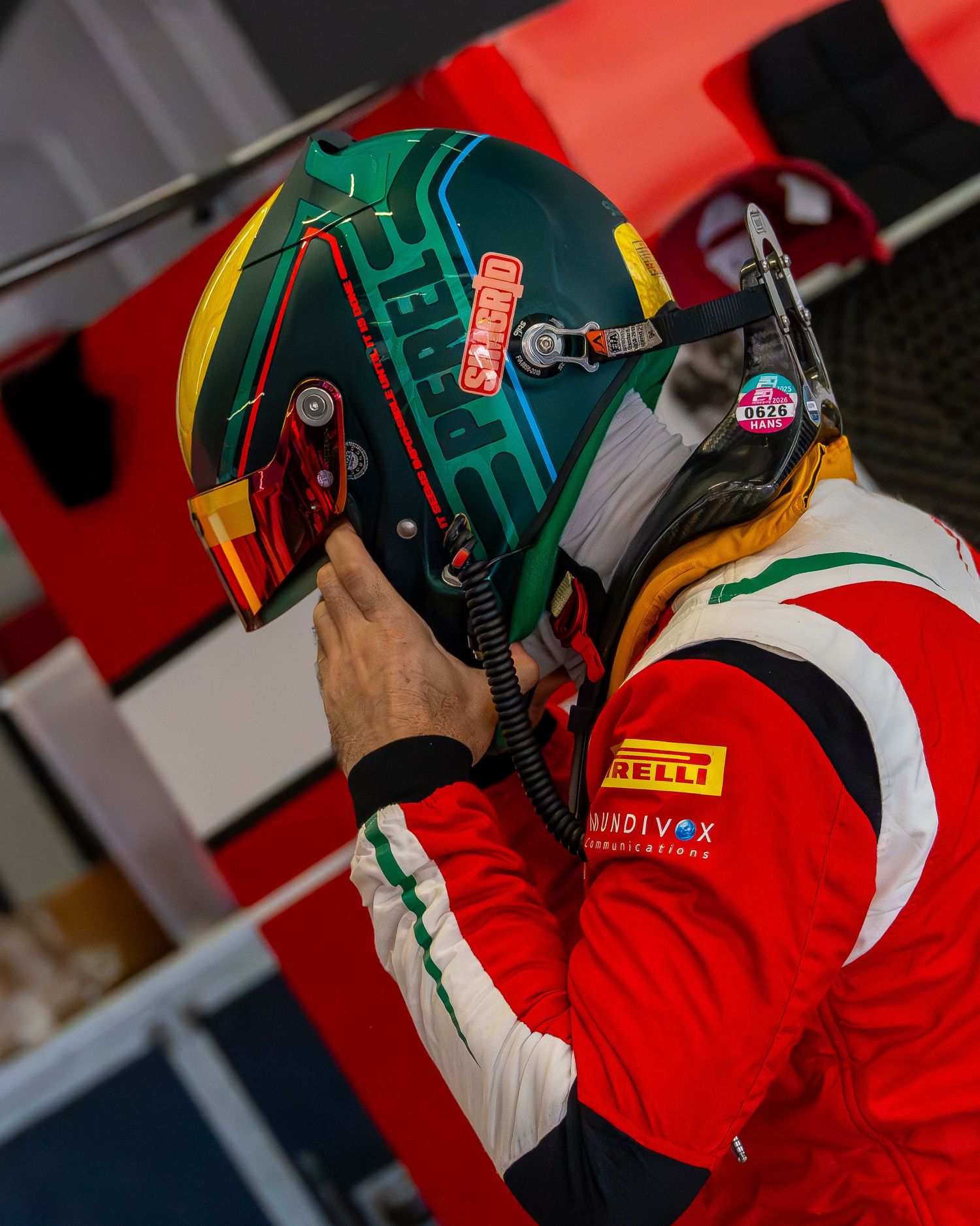 A driver in a red racing suit adjusts his helmet before the race.