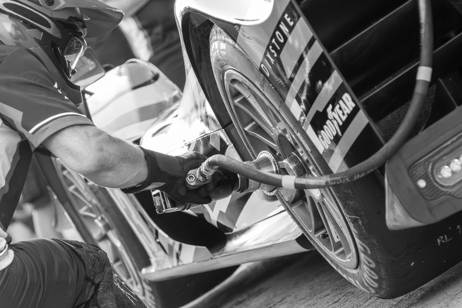 Close-up of a mechanic changing a racing car tire during a fast pit stop, dramatic black and white photography.