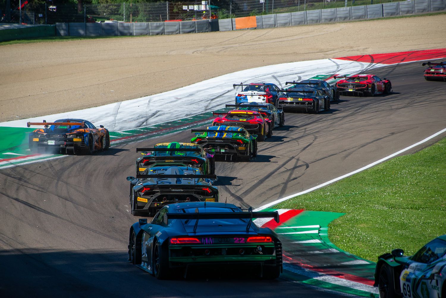 A large pack of GT3 sports cars racing closely in a line through Acque Minerali at Imola circuit.