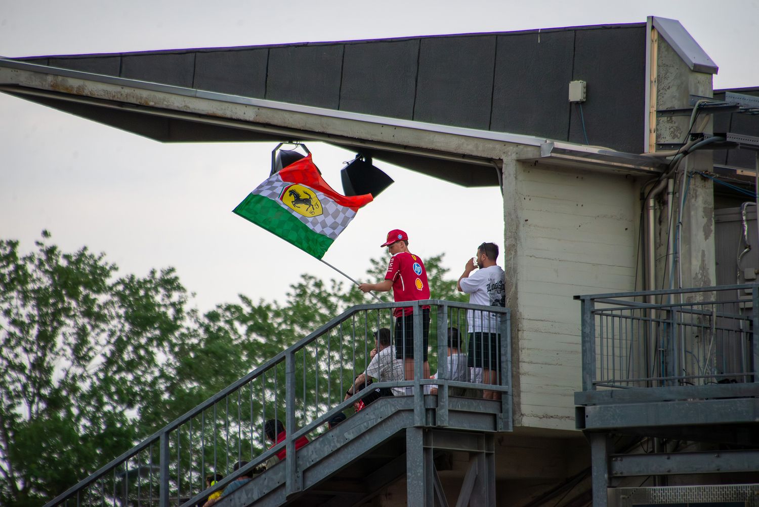 Ferrari fan waving a flag from a grandstand structure at Imola circuit.