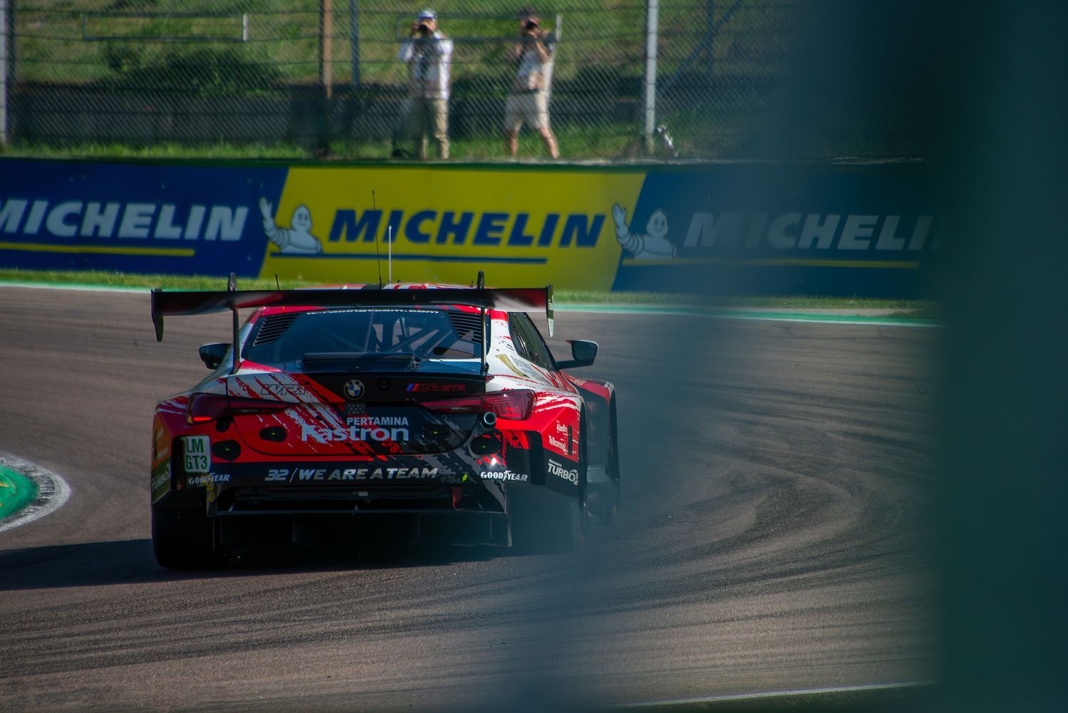Rear view of a BMW M4 GT3 race car driving down the track past yellow Michelin banners at Imola.