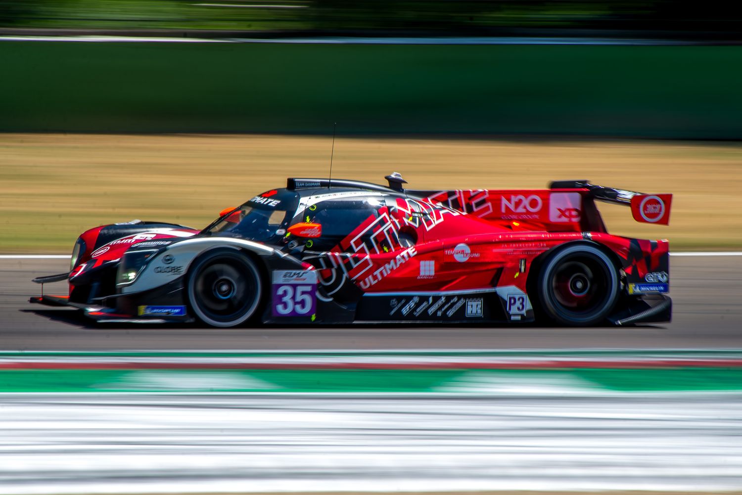 Side profile panning shot of the red and black number 35 prototype racing car speeding down the main straight.
