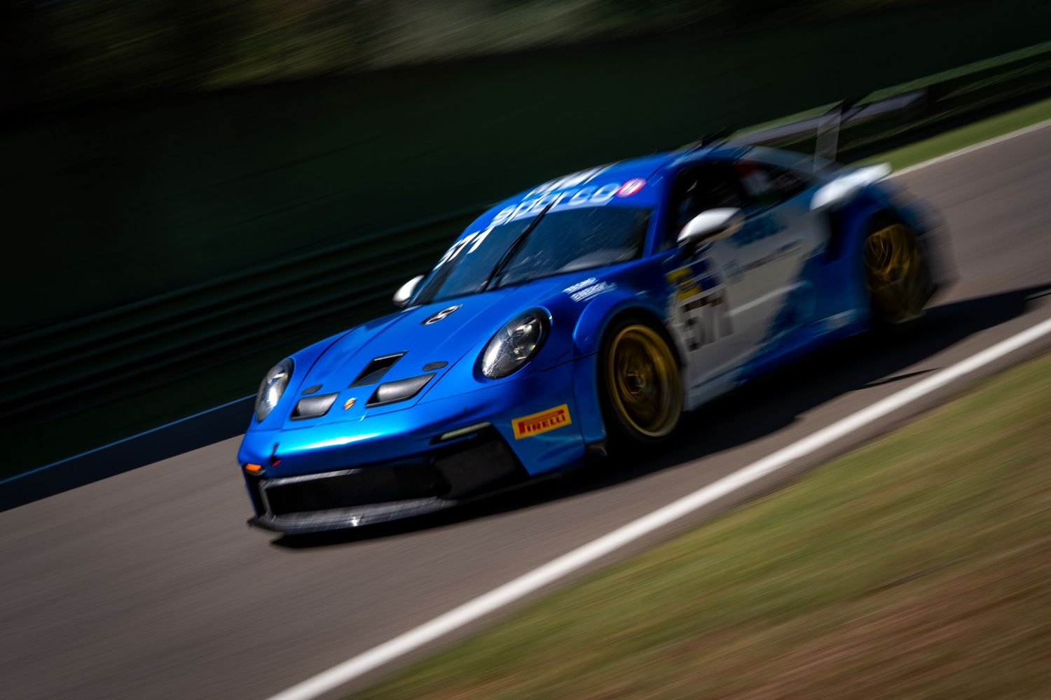 Blue Porsche GT3 speeding through Imola with motion blur and a grassy background.