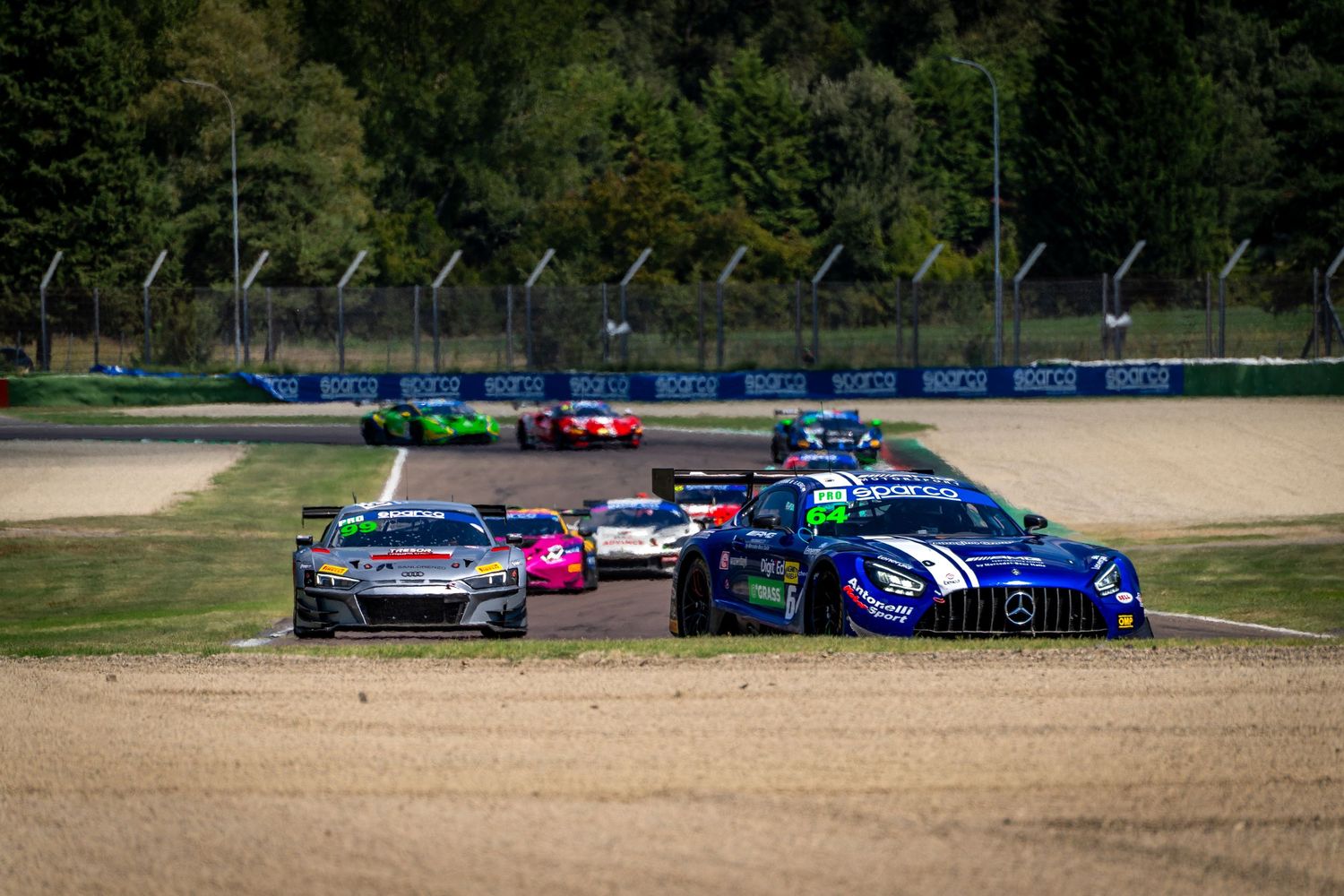 GT cars battling closely together through a gravel-lined section of Imola, with several cars packed into the corner.