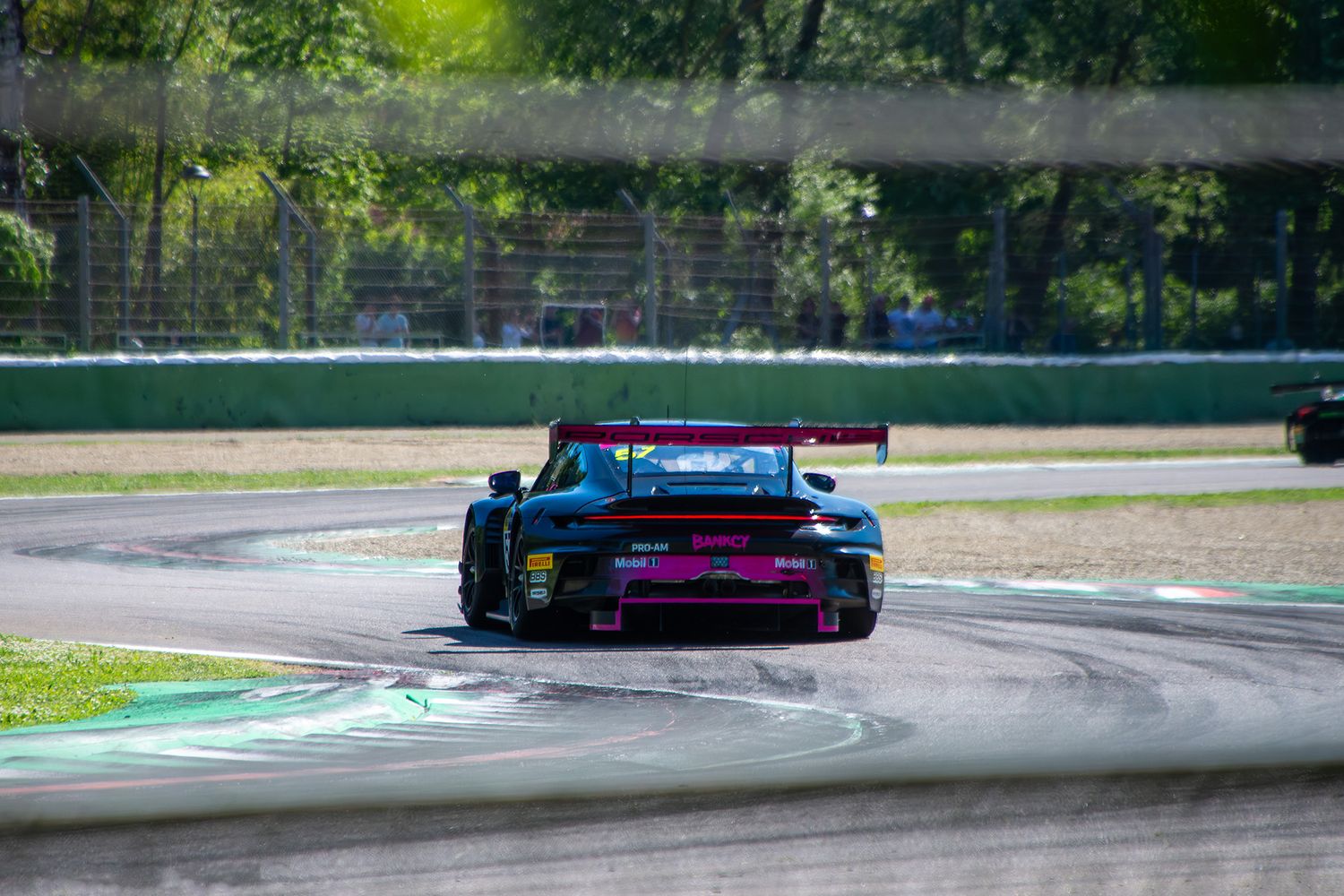 Porsche GT3 racing car speeding past a safety catch fence with green trees in the background.
