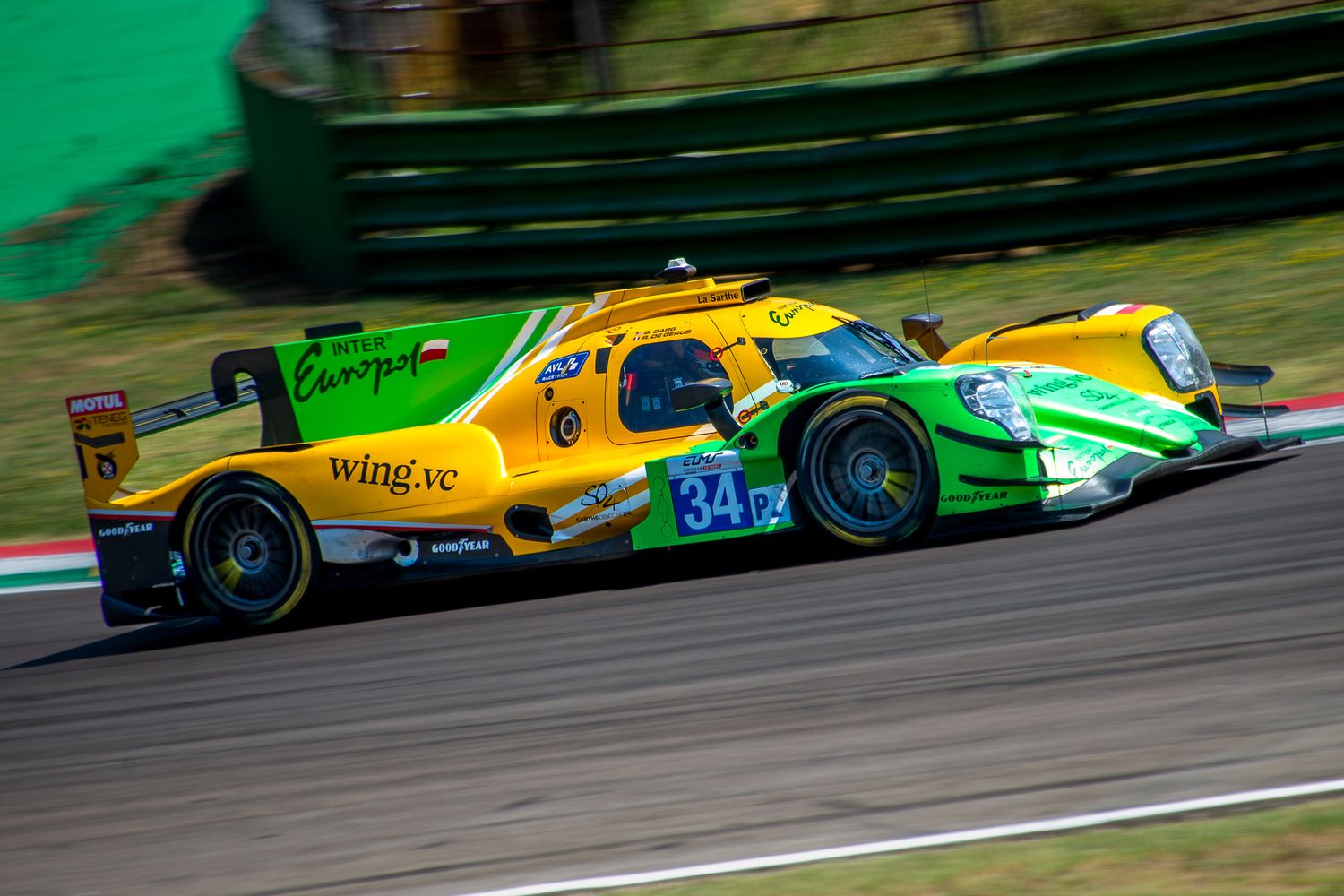 Yellow and green endurance prototype racing car number 34 speeding through a curve on a sunny racetrack.