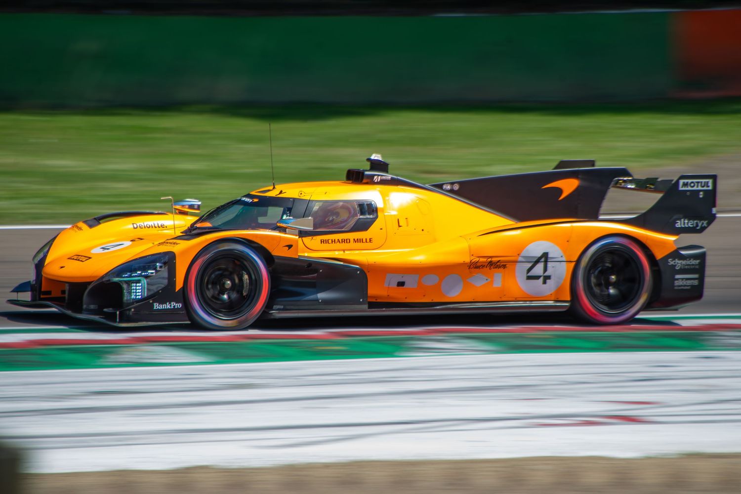 Side profile panning shot of the orange number 4 prototype racing car speeding down the track straightaway.