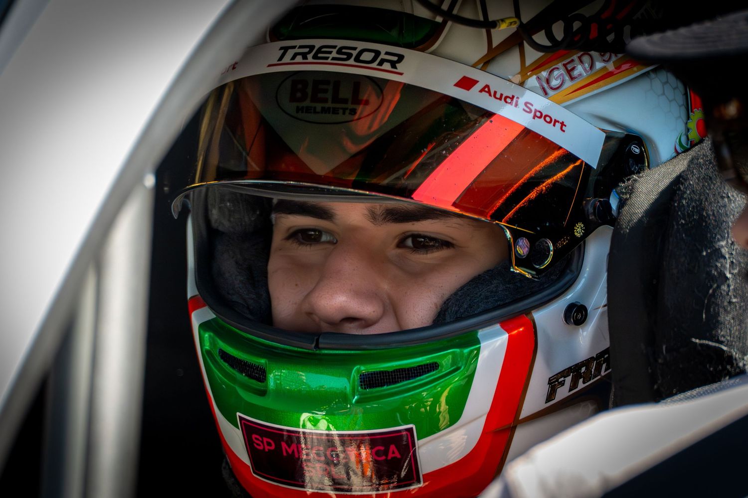 Driver wearing a helmet inside a race car, focused before the start.