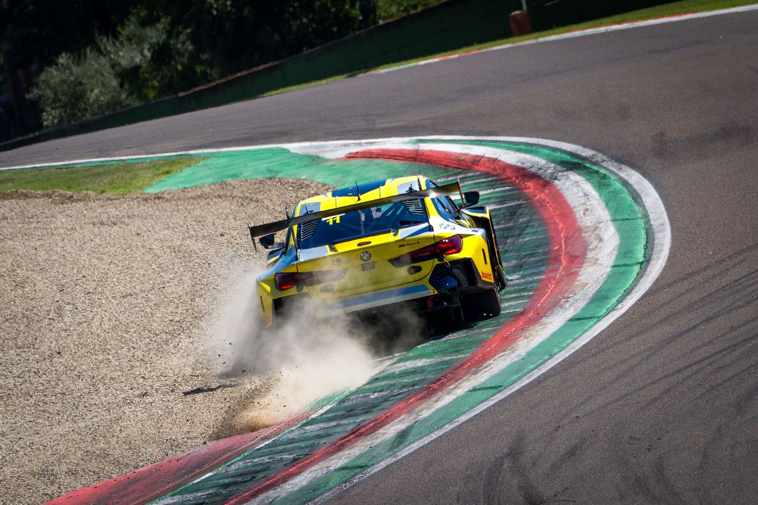 Yellow GT car kicking up dust as it runs wide over the kerbs at Imola.