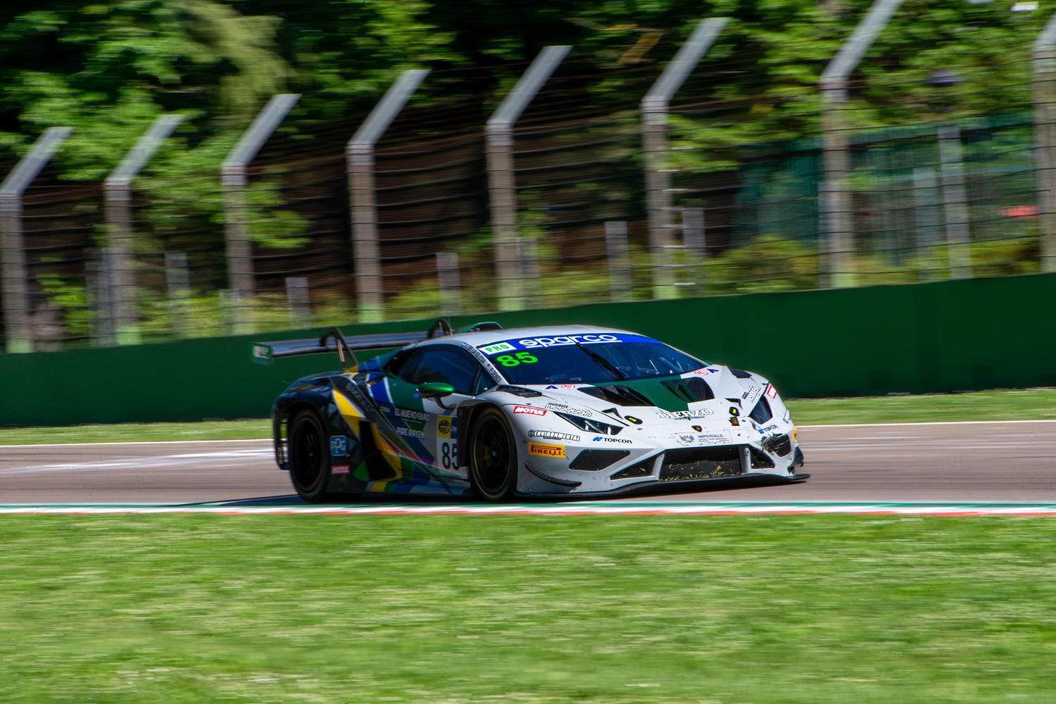 White and green Lamborghini Huracán GT3 racing car in a sharp panning shot past track fencing.