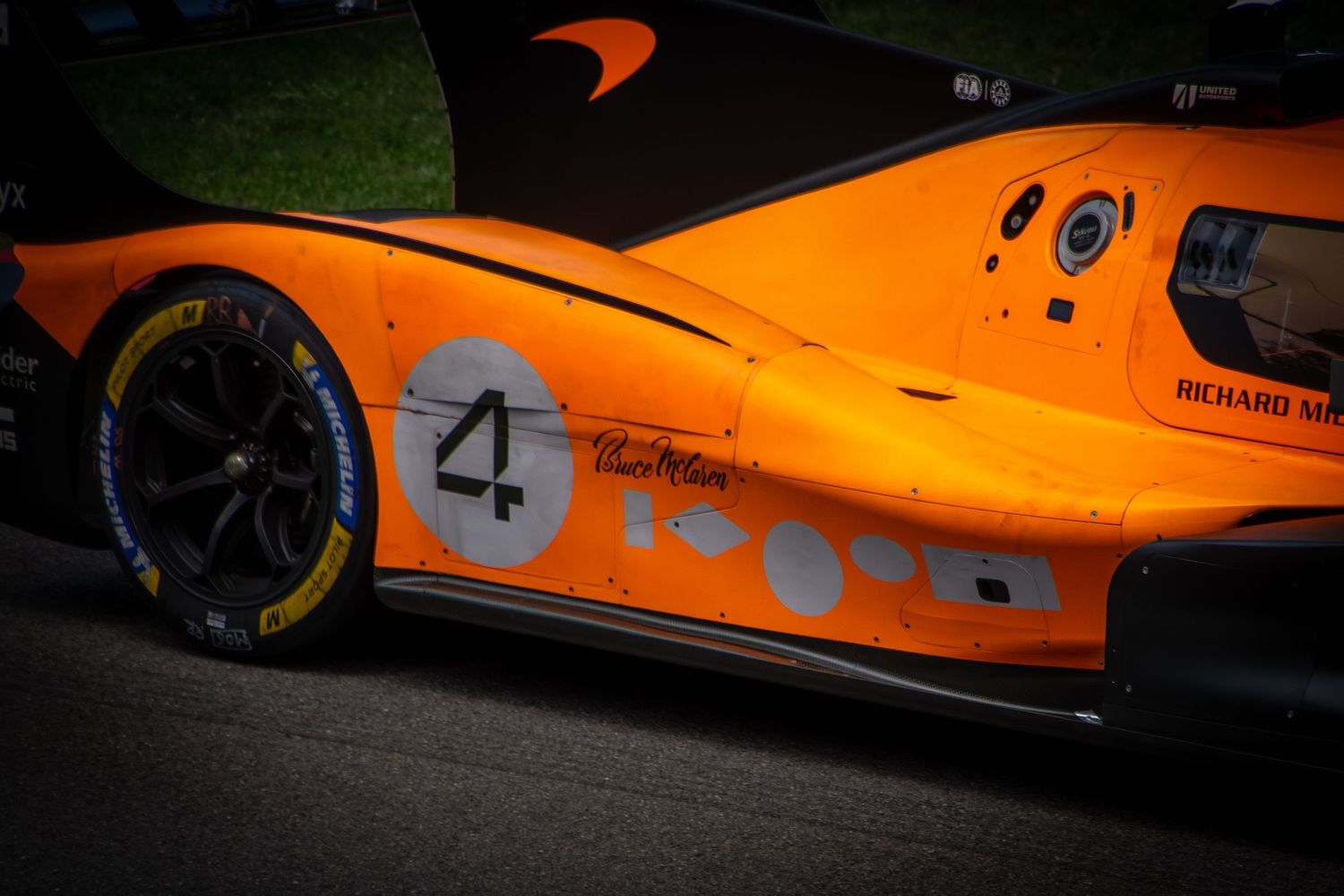 A close-up detail shot focusing on the side of the McLaren Solus GT, highlighting the vibrant papaya paintwork, a '4' decal, intricate side
